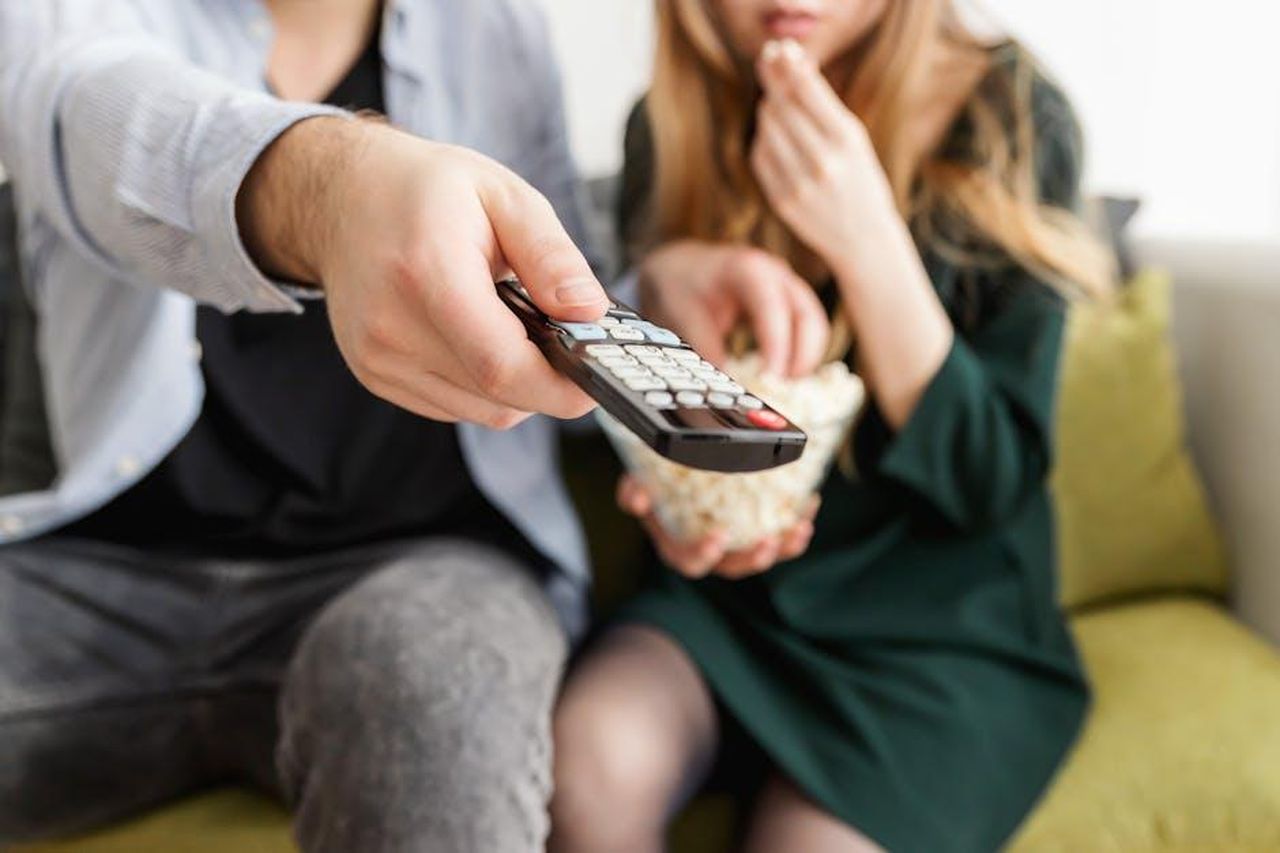 Source: JESHOOTS.com - pexels - A couple enjoying a relaxing movie night, sitting on a sofa with popcorn and a TV remote.