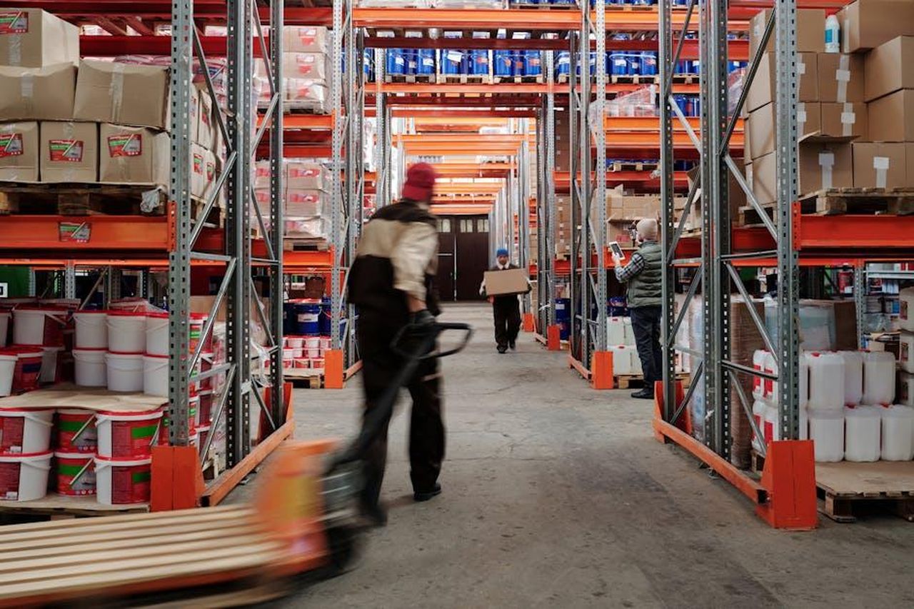Source: Tiger Lily - pexels - Warehouse interior with workers organizing shelves full of boxes and containers.