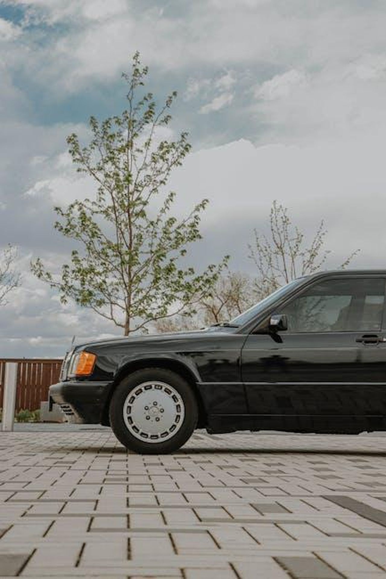 Source: Jacob Moore - pexels - Elegant black luxury car parked outdoors on a paved road with sky and tree background.