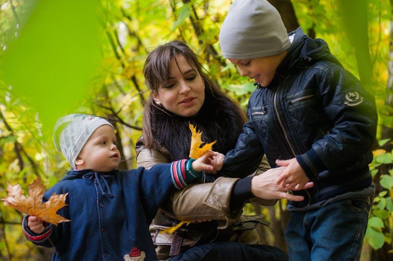 Source: Berendey_Ivanov / Andrey_Kobysnyn - pexels - Joyful family moment in park with kids playing among colorful autumn leaves.