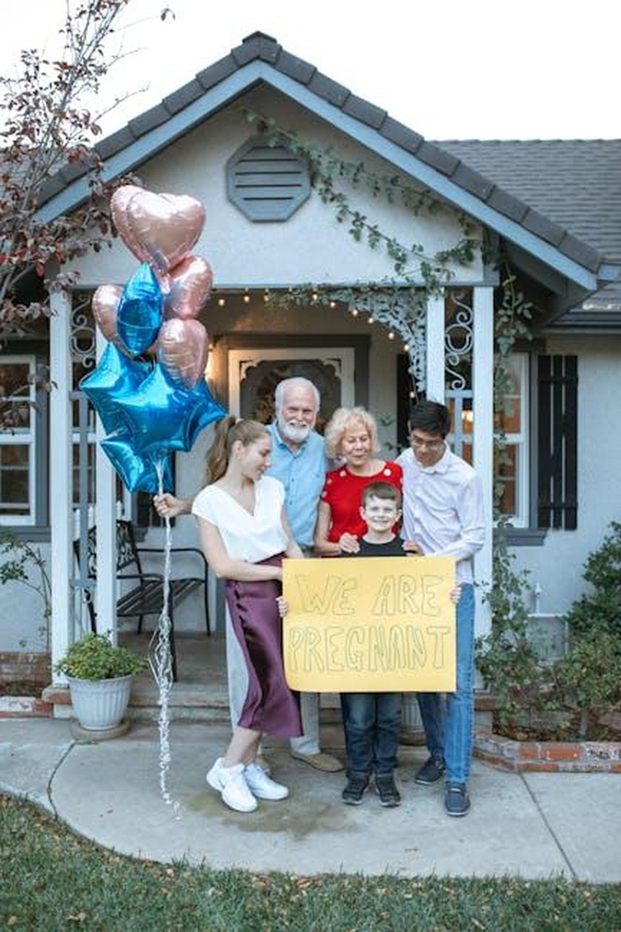 Source: RDNE Stock project - pexels - A family joyfully announces a pregnancy with a sign and balloons outside their home.