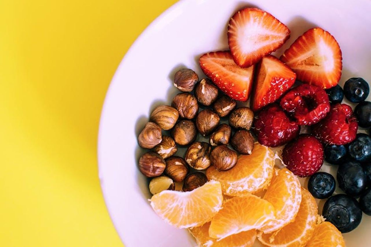 Source: Lisa Fotios - pexels - Close-up of a bowl with fresh fruits and nuts against a vibrant yellow backdrop.