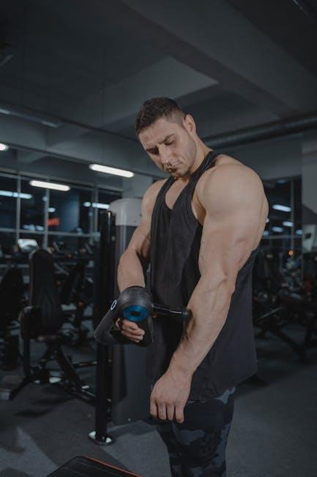 Source: Tima Miroshnichenko - pexels - A muscular man uses a massage gun in a gym, showcasing fitness and recovery.