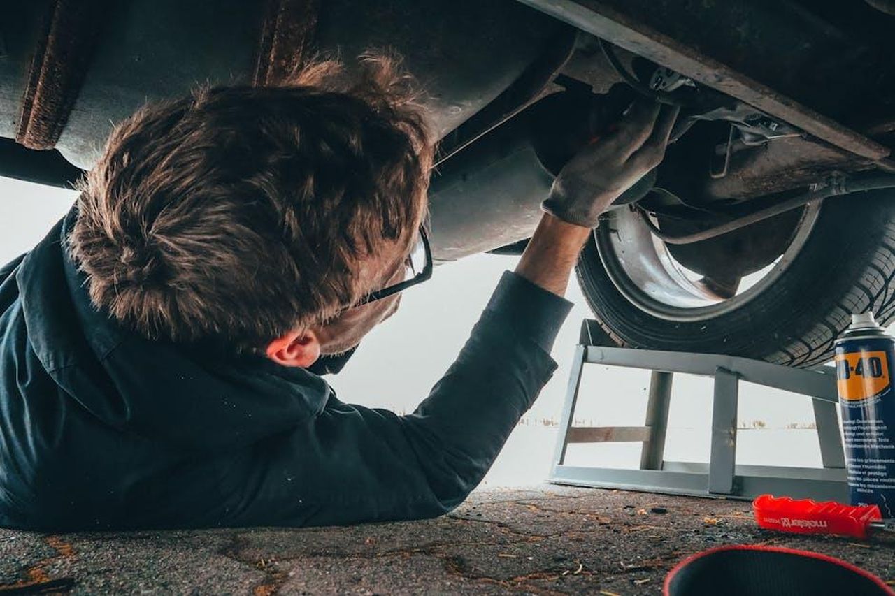 Source: Malte Luk - pexels - Mechanic skillfully repairing car undercarriage in outdoor setting with tools.