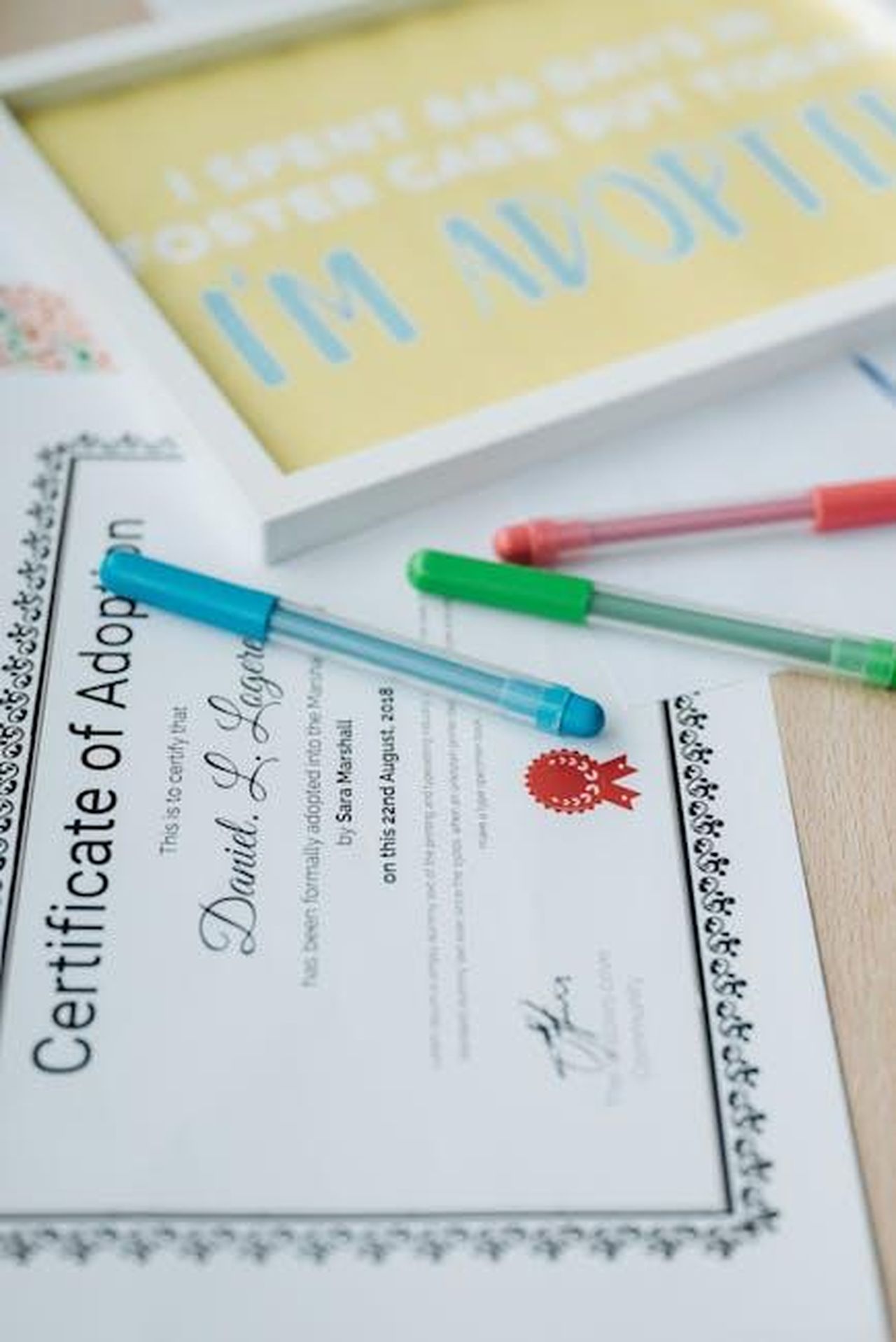 Source: Pavel Danilyuk - pexels - Close-up of an adoption certificate with colorful pens and an adoption-themed frame.