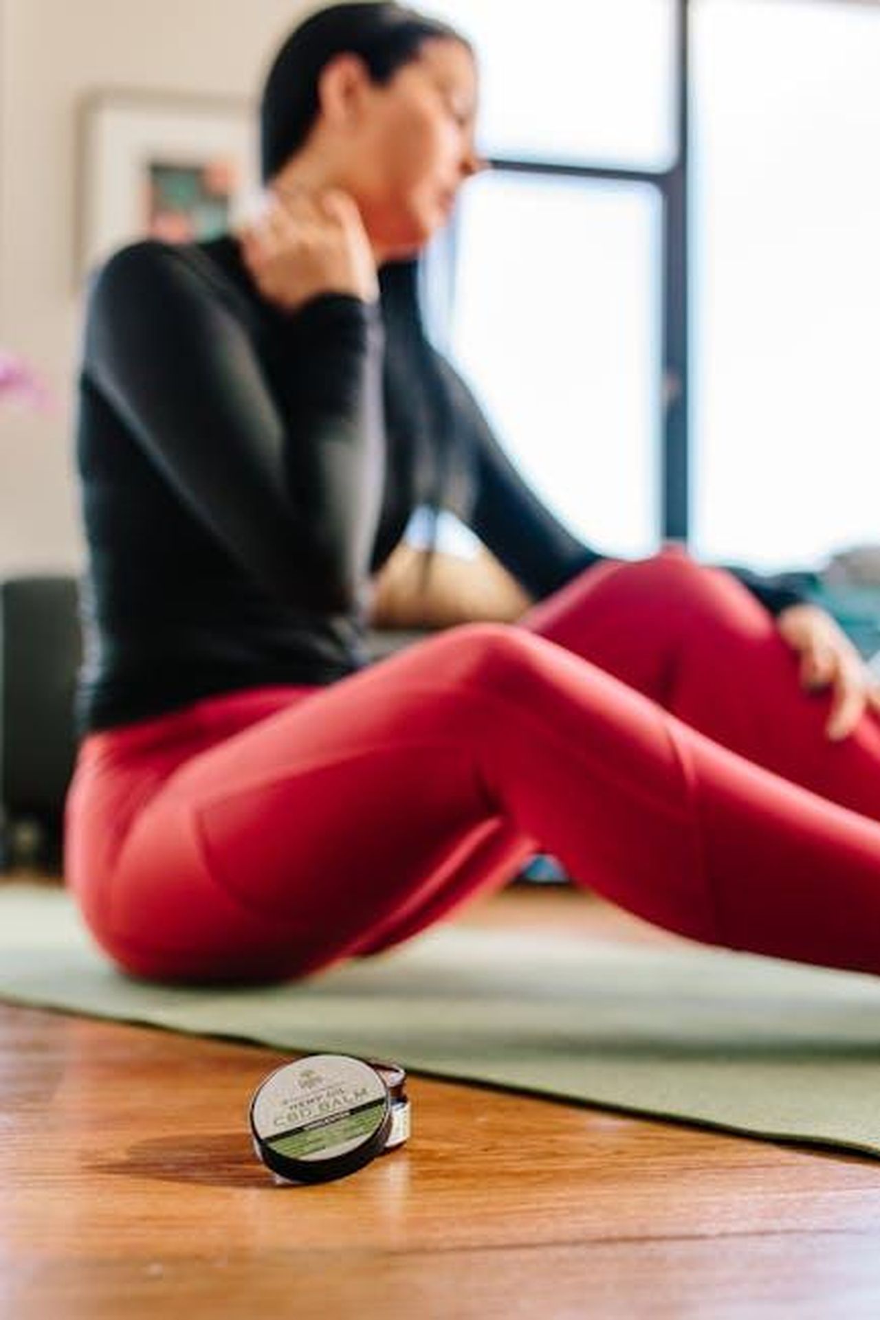 Source: Tree of Life Seeds - pexels - A woman sitting on a yoga mat indoors, using CBD cream for neck pain relief after exercise.