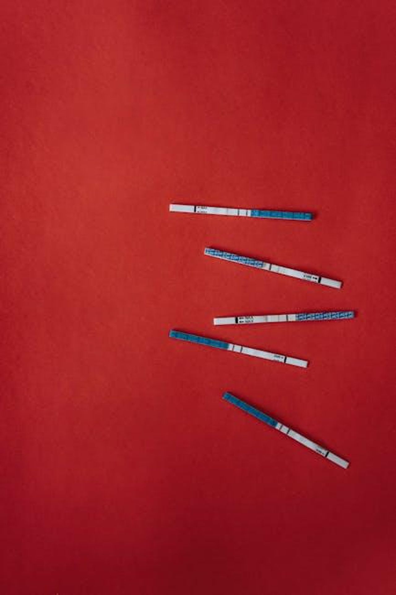 Source: olia danilevich - pexels - Pregnancy test strips arranged on a vivid red background, symbolizing health and biology.