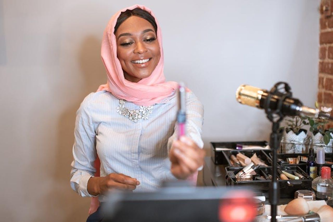 Source: RDNE Stock project - pexels - A smiling Muslim woman wearing a hijab records a makeup tutorial for her vlog.