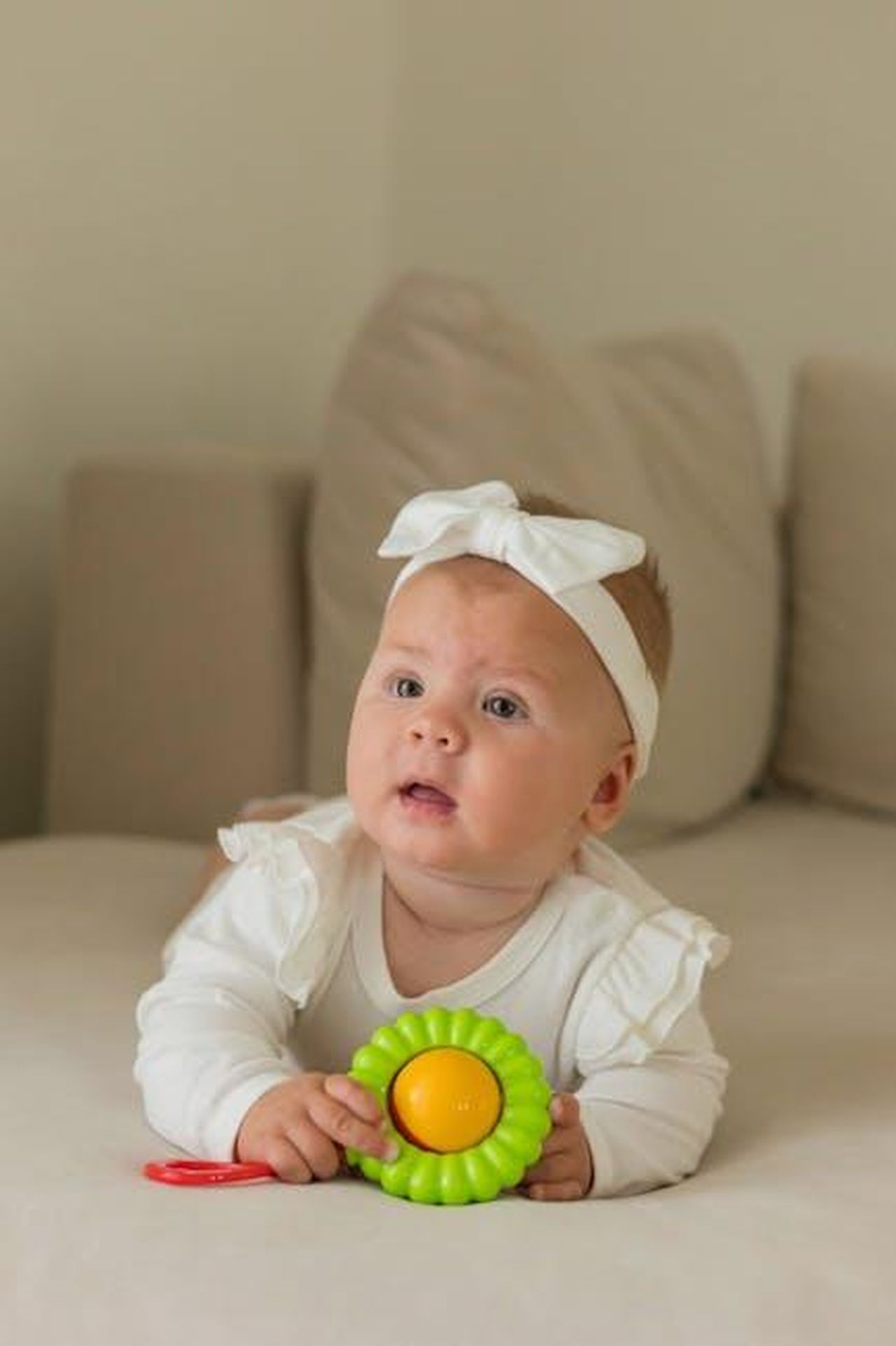 Source: Polesie Toys - pexels - Cute baby in white outfit holding a colorful toy while lying on a beige couch. Perfect for lifestyle imagery.