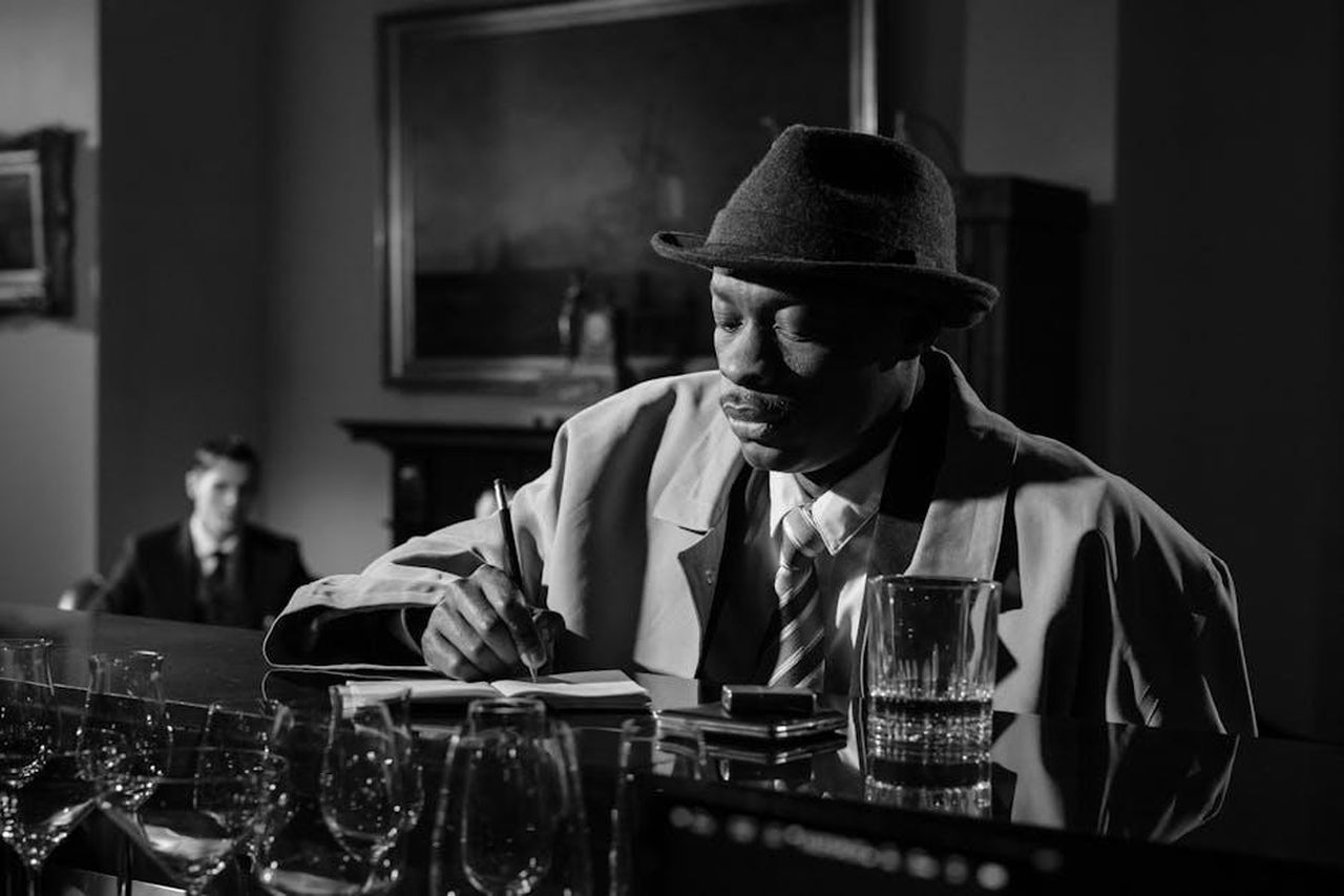 Source: cottonbro studio - pexels - A classic noir scene with a detective taking notes in a dimly lit bar, emphasizing mystery and intrigue.