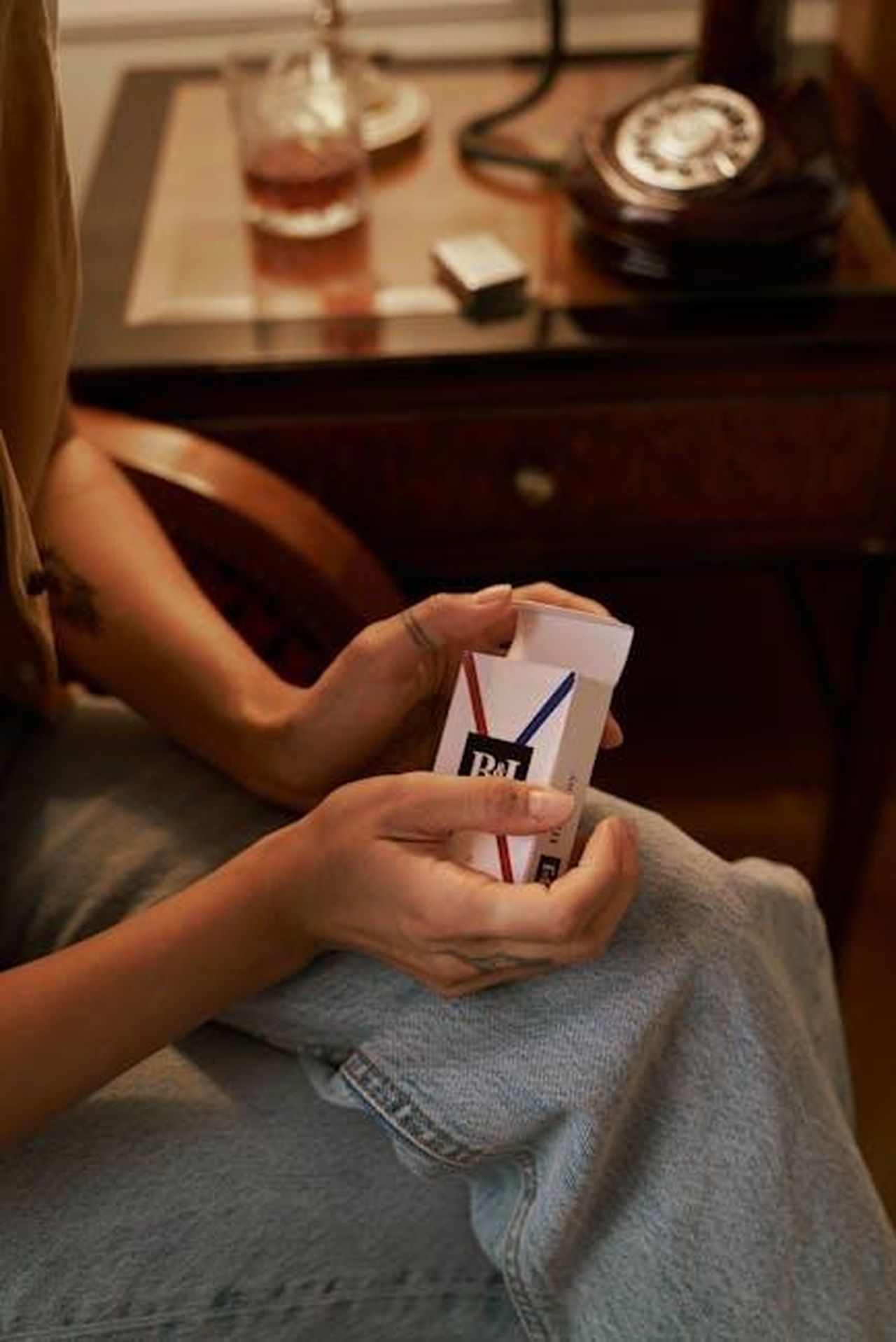 Source: Ron Lach - pexels - Woman holding a cigarette packet, sitting in relaxed indoor setting.