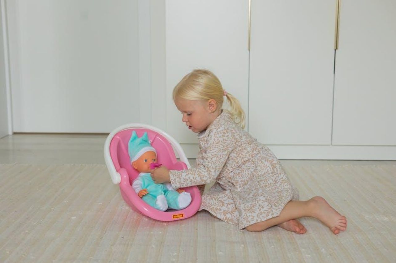 Source: Polesie Toys - pexels - A young girl in a floral dress playing with a baby doll on the floor indoors.