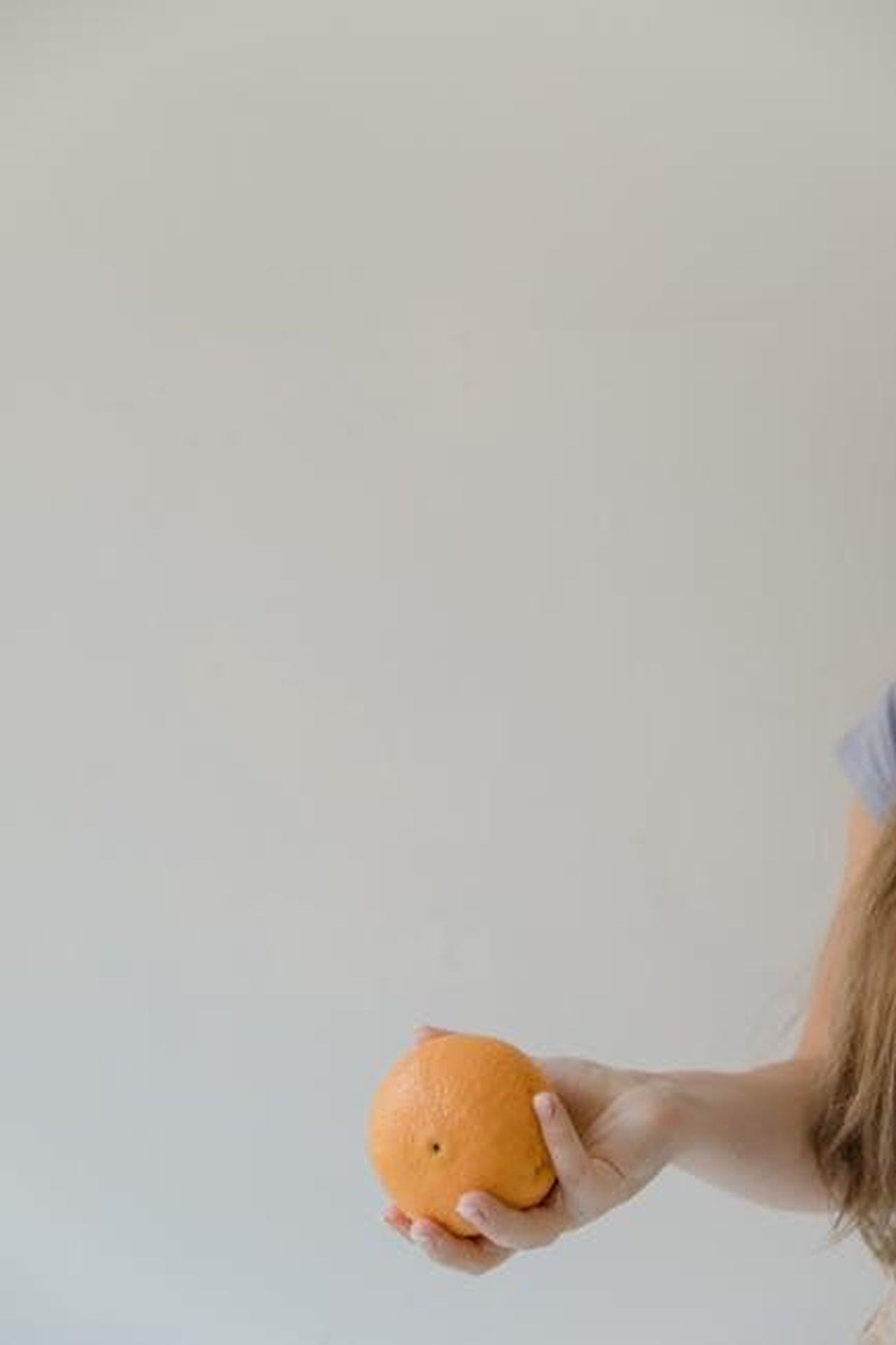 Source: RDNE Stock project - pexels - A close-up shot of a hand holding a fresh orange against a neutral background.