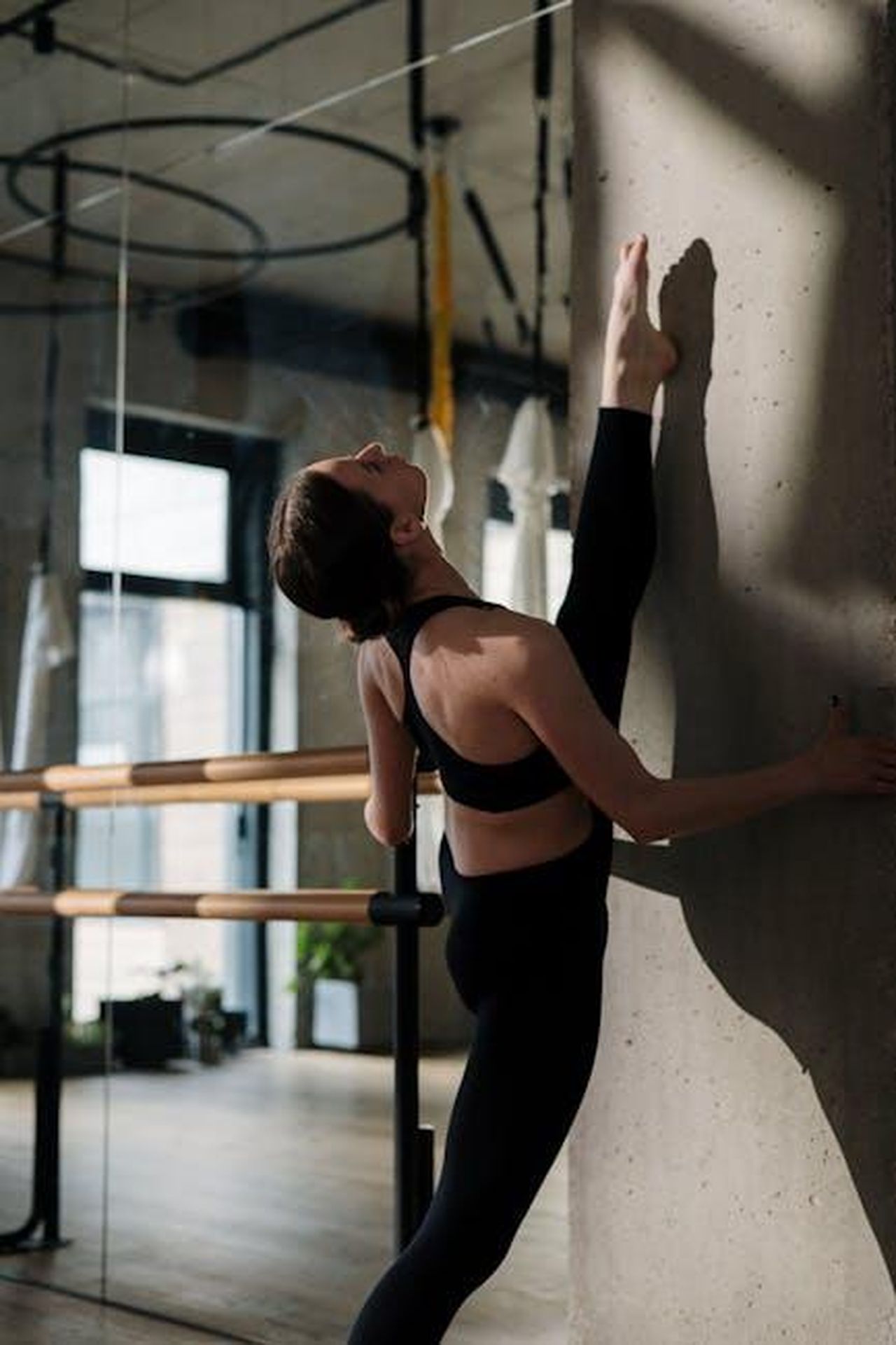 Source: cottonbro studio - pexels - A woman stretches against a concrete wall in a bright yoga studio, demonstrating flexibility.