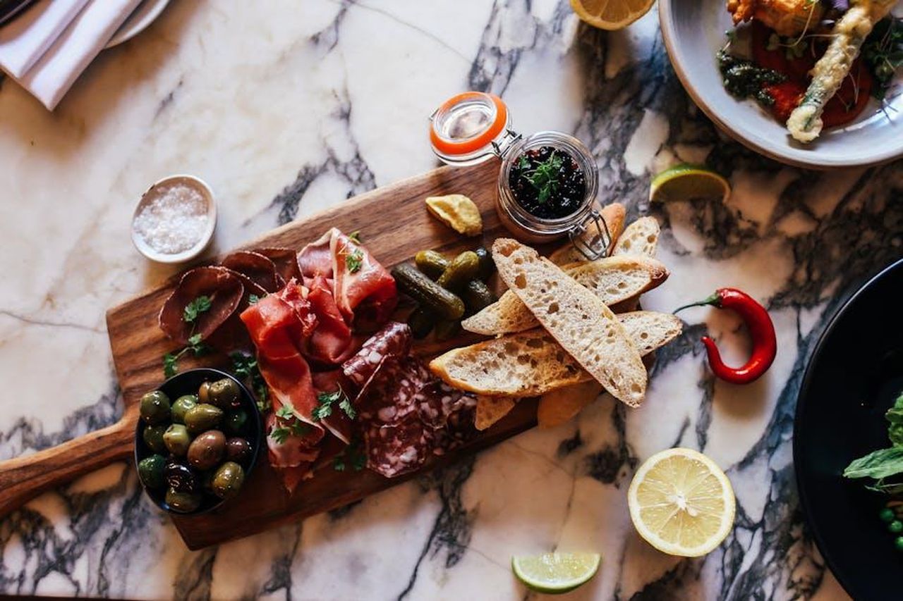 Source: Rachel Claire - pexels - A rustic charcuterie board with meats, olives, and bread on a marble table.