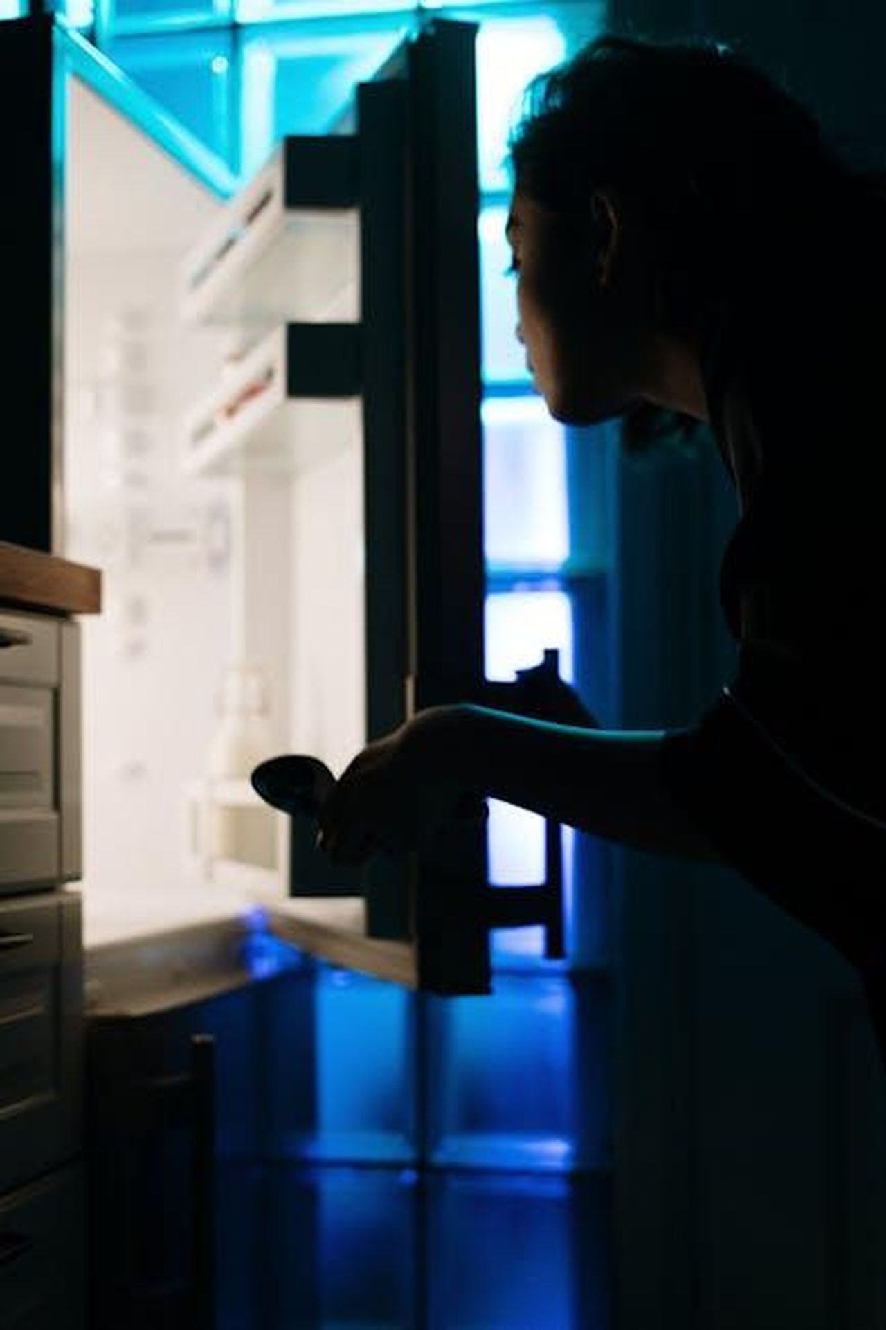 Source: cottonbro studio - pexels - Silhouette of a woman checking an empty fridge at night with neon light.
