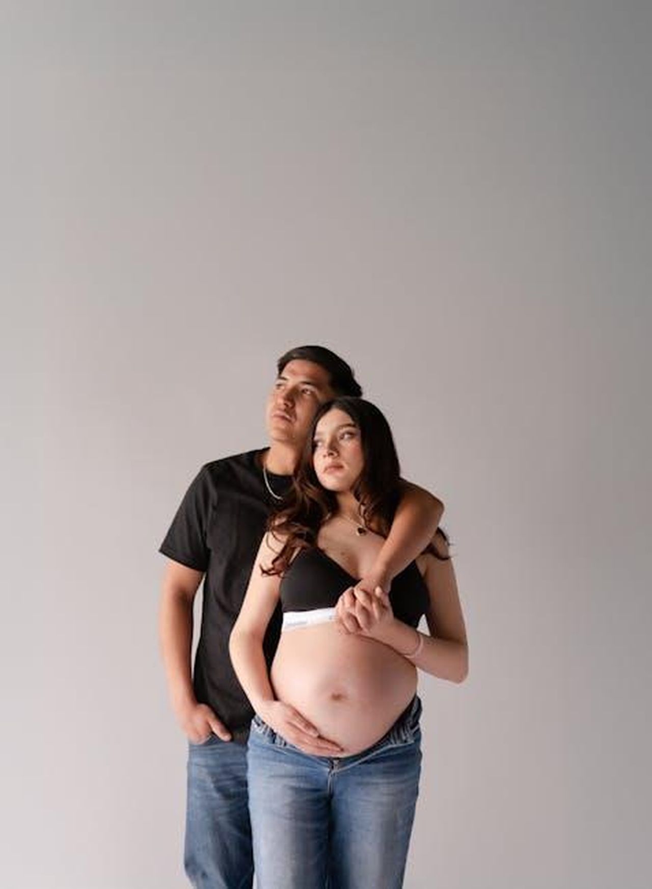 Source: Carlos Santiago - pexels - Expecting couple in casual jeans, embracing in a light studio setting, conveying love and anticipation.