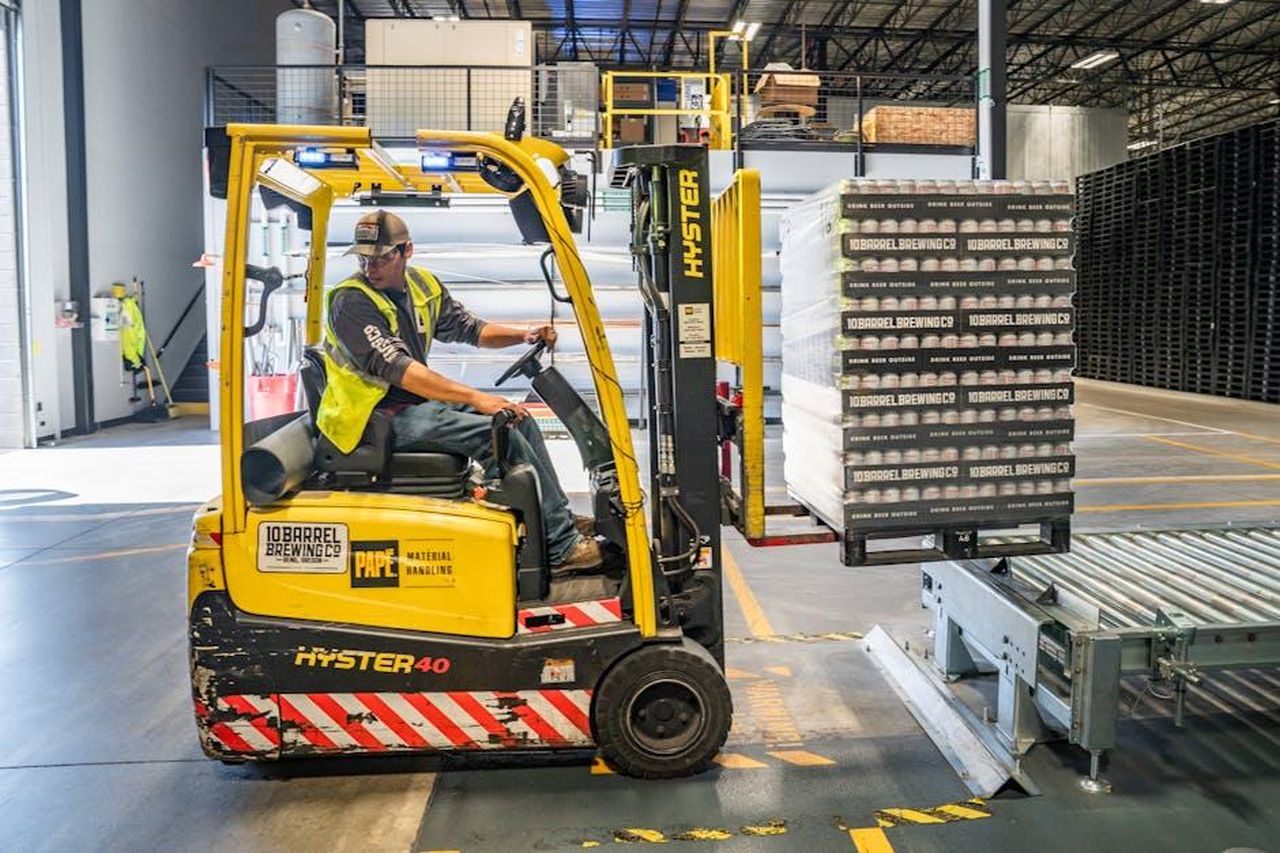 Source: ELEVATE - pexels - A warehouse worker maneuvers a forklift to transport crates for brewing company storage.