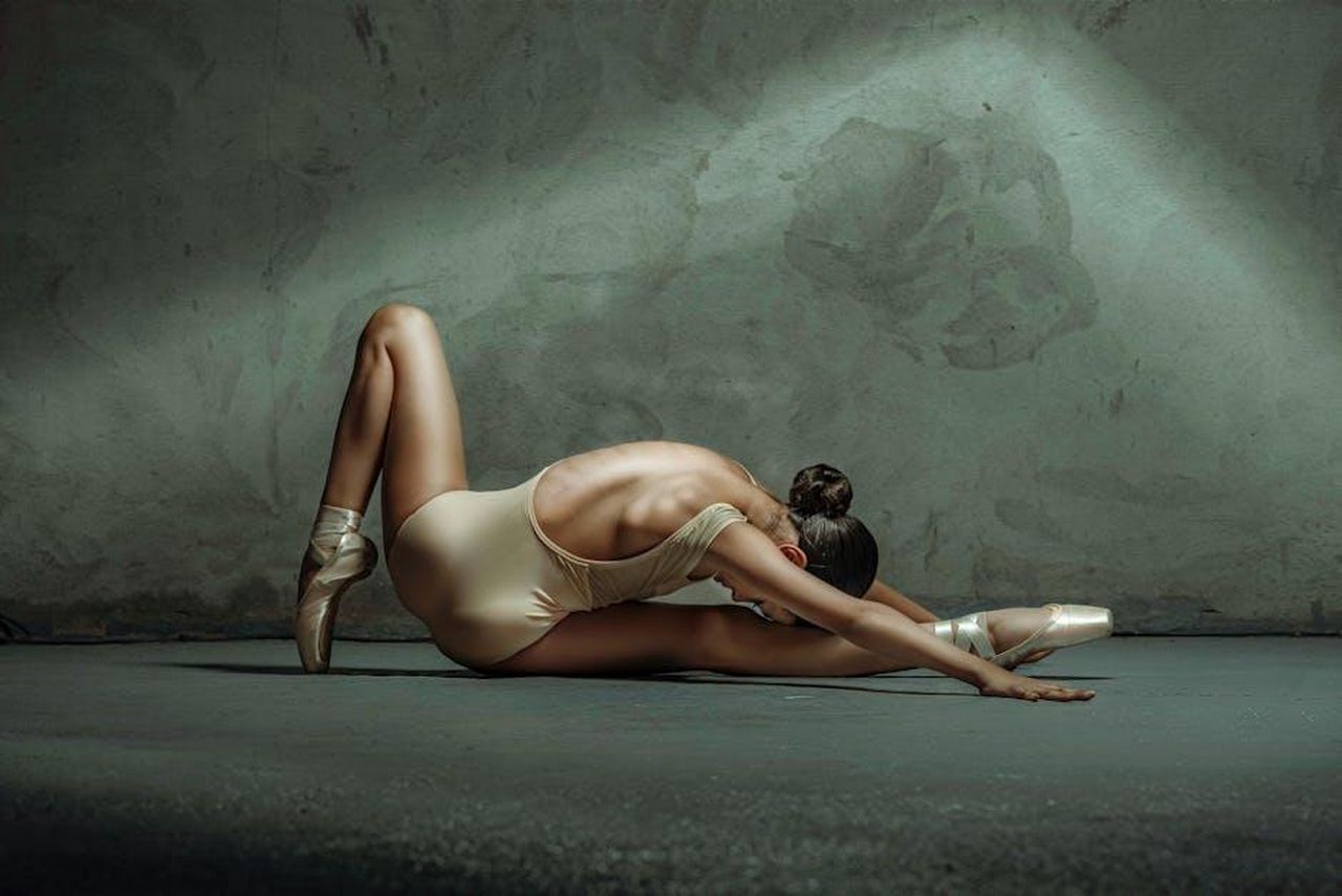 Source: Natalia Olivera - pexels - Graceful ballerina stretches elegantly in a dimly lit dance studio, showcasing flexibility and poise.