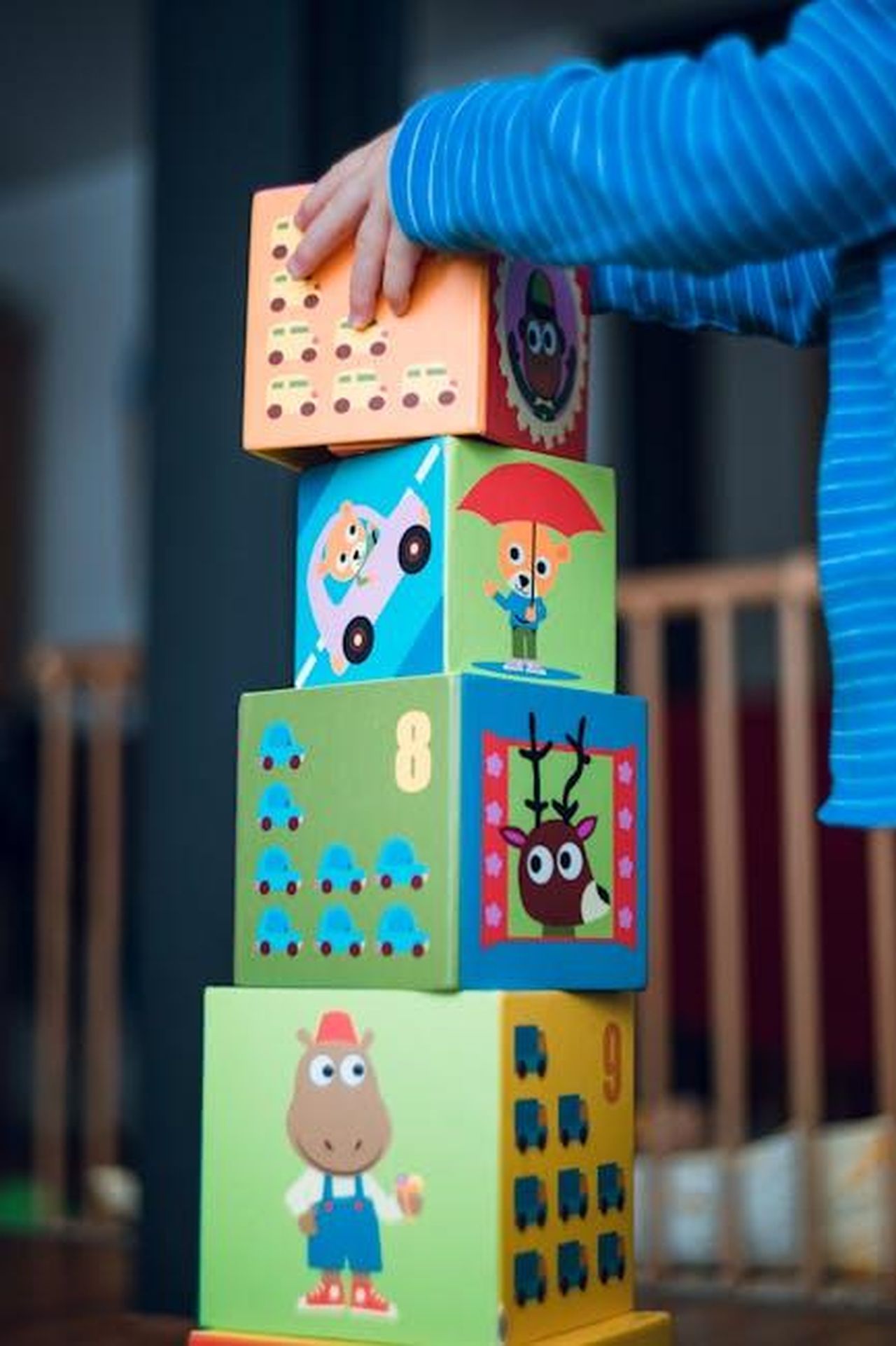 Source: Markus Spiske - pexels - A child playing indoors, stacking colorful wooden toy blocks with joyful illustrations.