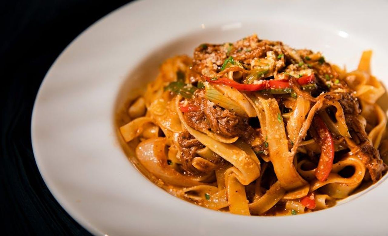 Source: Change C.C - pexels - Savory beef tagliatelle pasta with peppers and herbs in a white plate, perfect for a gourmet meal.
