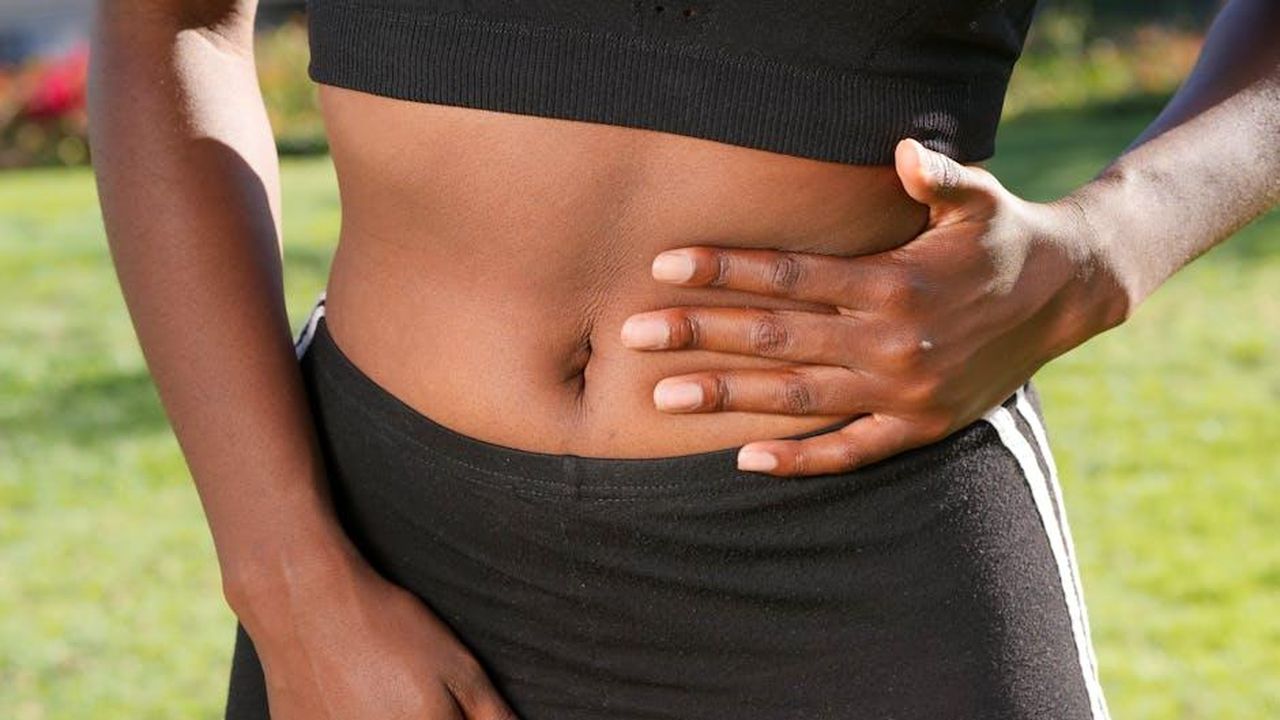 Source: Kindel Media - pexels - Close-up of a person holding their abdomen, indicating stomach discomfort, outdoors.
