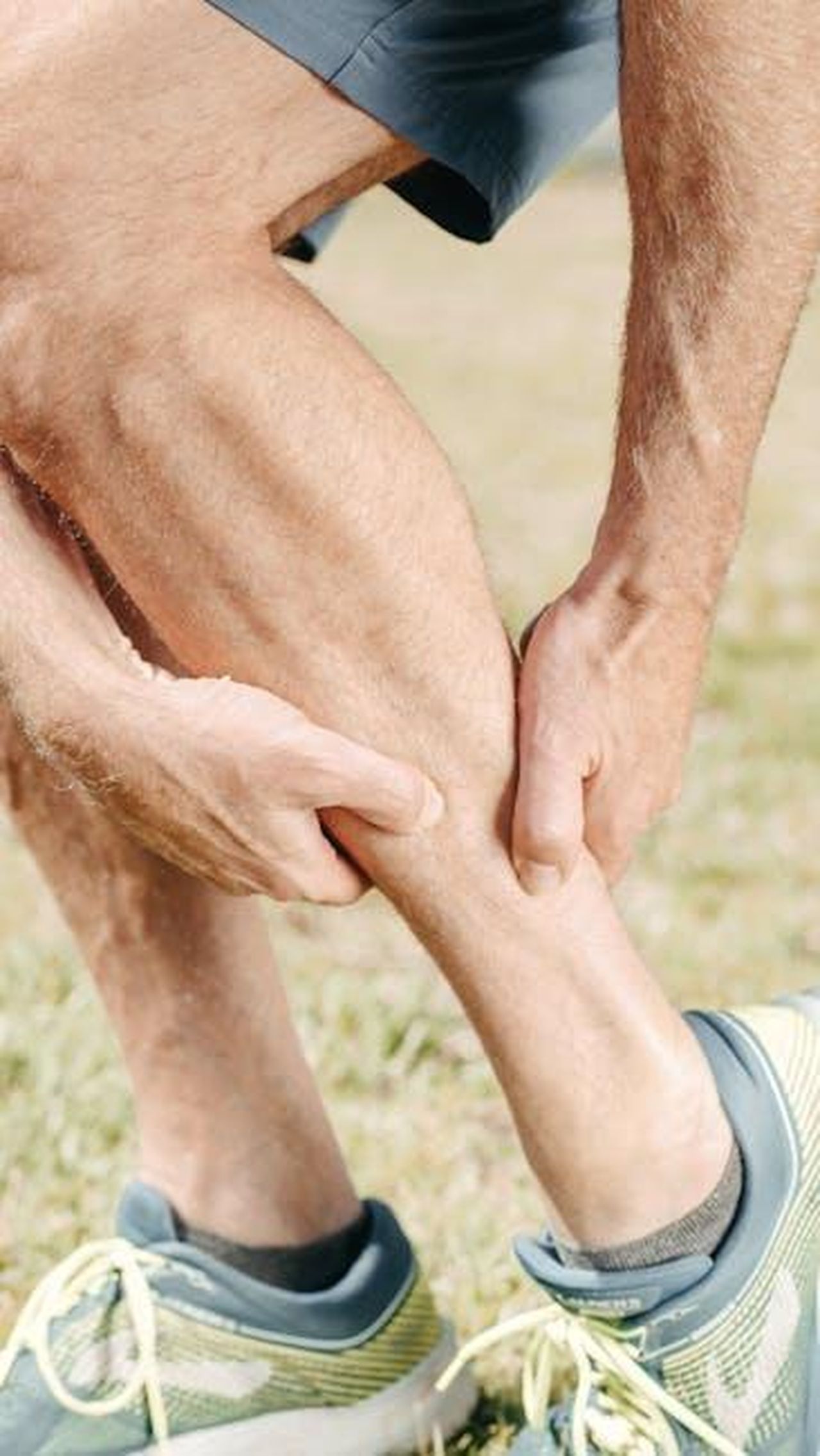 Source: Kindel Media - pexels - A man outdoors massaging his calf, dealing with muscle pain during sports activities.