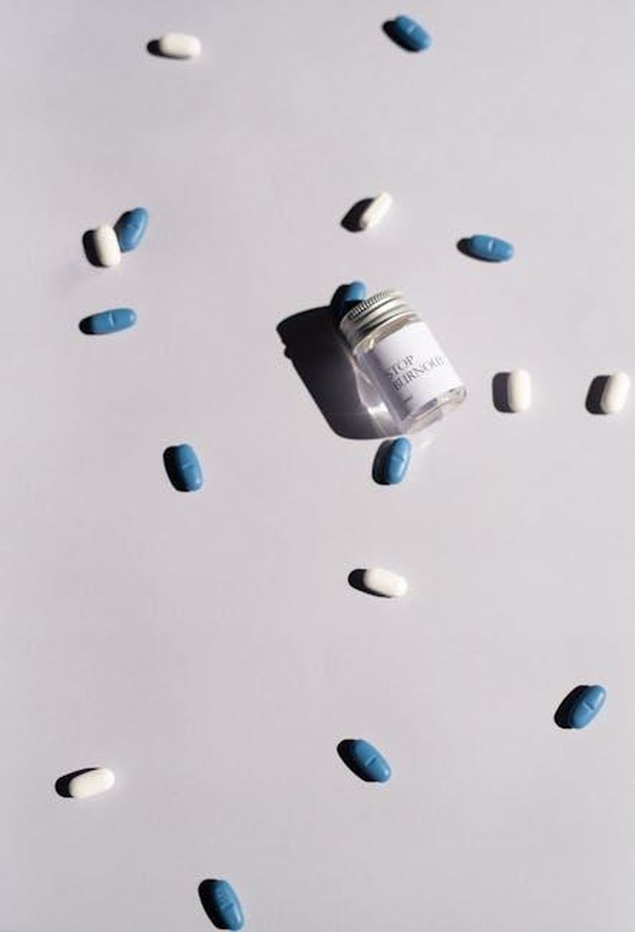 Source: Leeloo The First - pexels - Jar of pills and scattered blue and white tablets on a white surface, highlighting healthcare themes.
