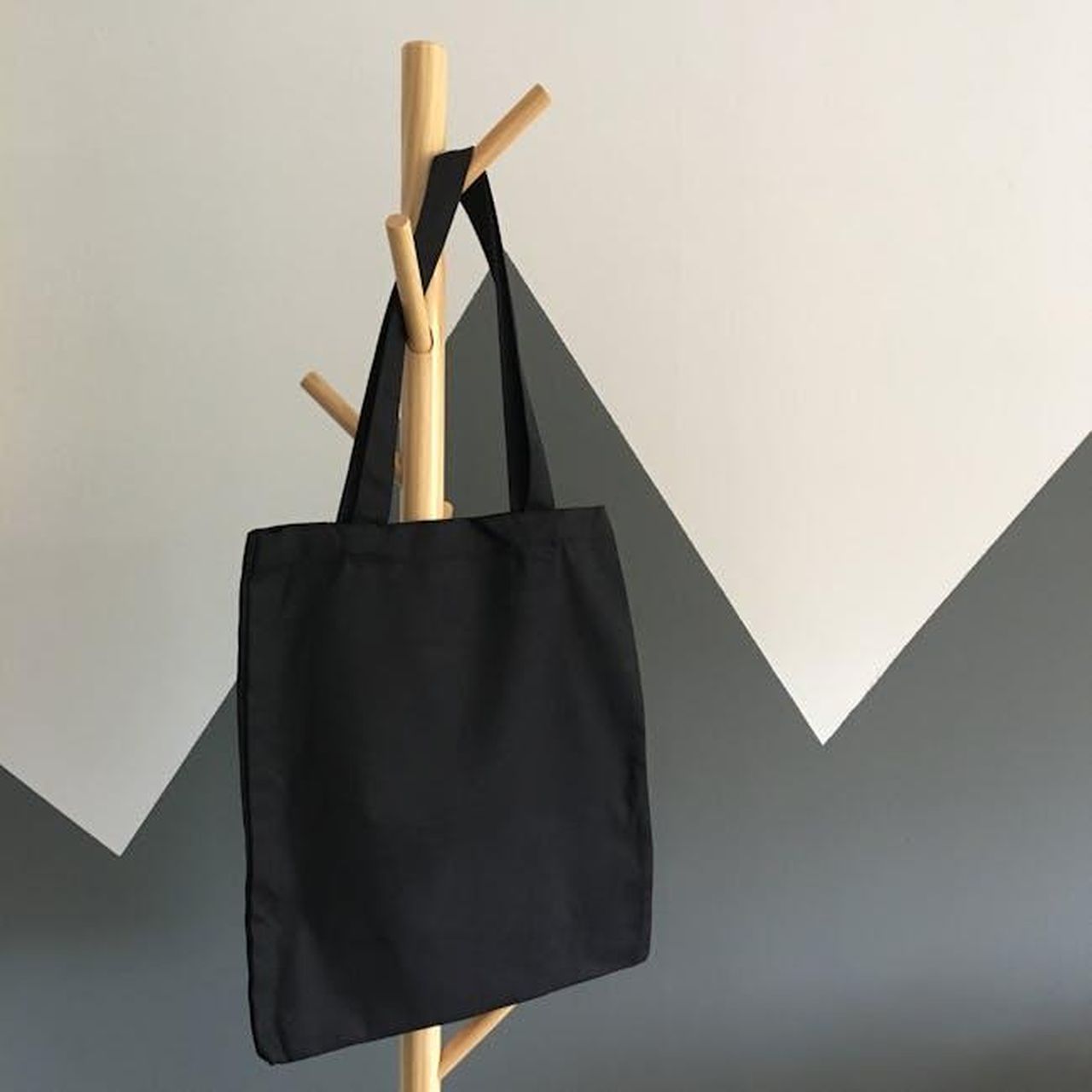 Source: Stephanie Ho - pexels - Simple and elegant black canvas tote bag hanging on a wooden rack, perfect for eco-friendly shopping.