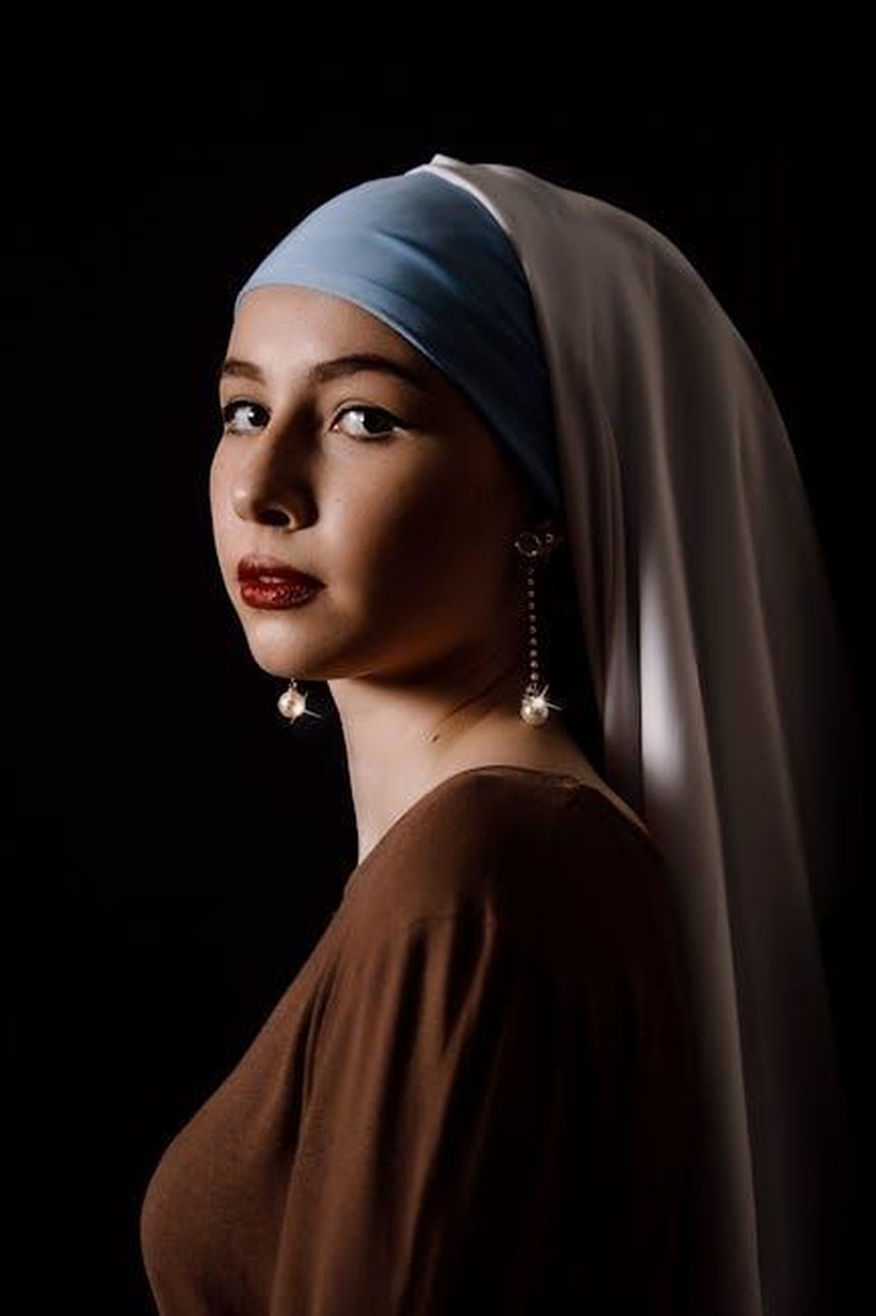 Source: Ibraim Leonardo - pexels - A woman in a headscarf and earrings poses gracefully in low light, showcasing elegance and poise.