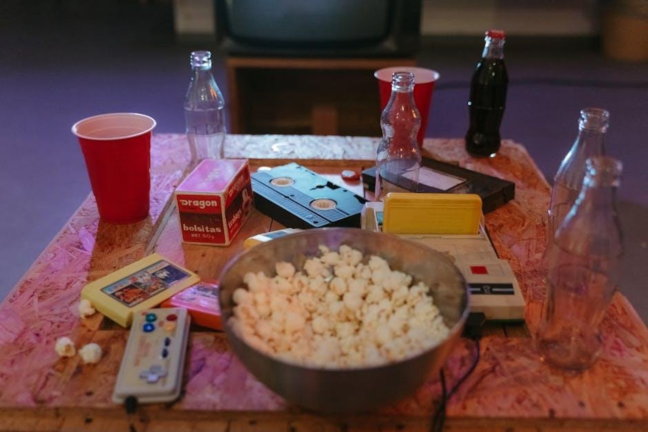 Source: MART  PRODUCTION - pexels - A nostalgic setup with popcorn, VHS tapes, and retro gaming consoles on a wooden table.