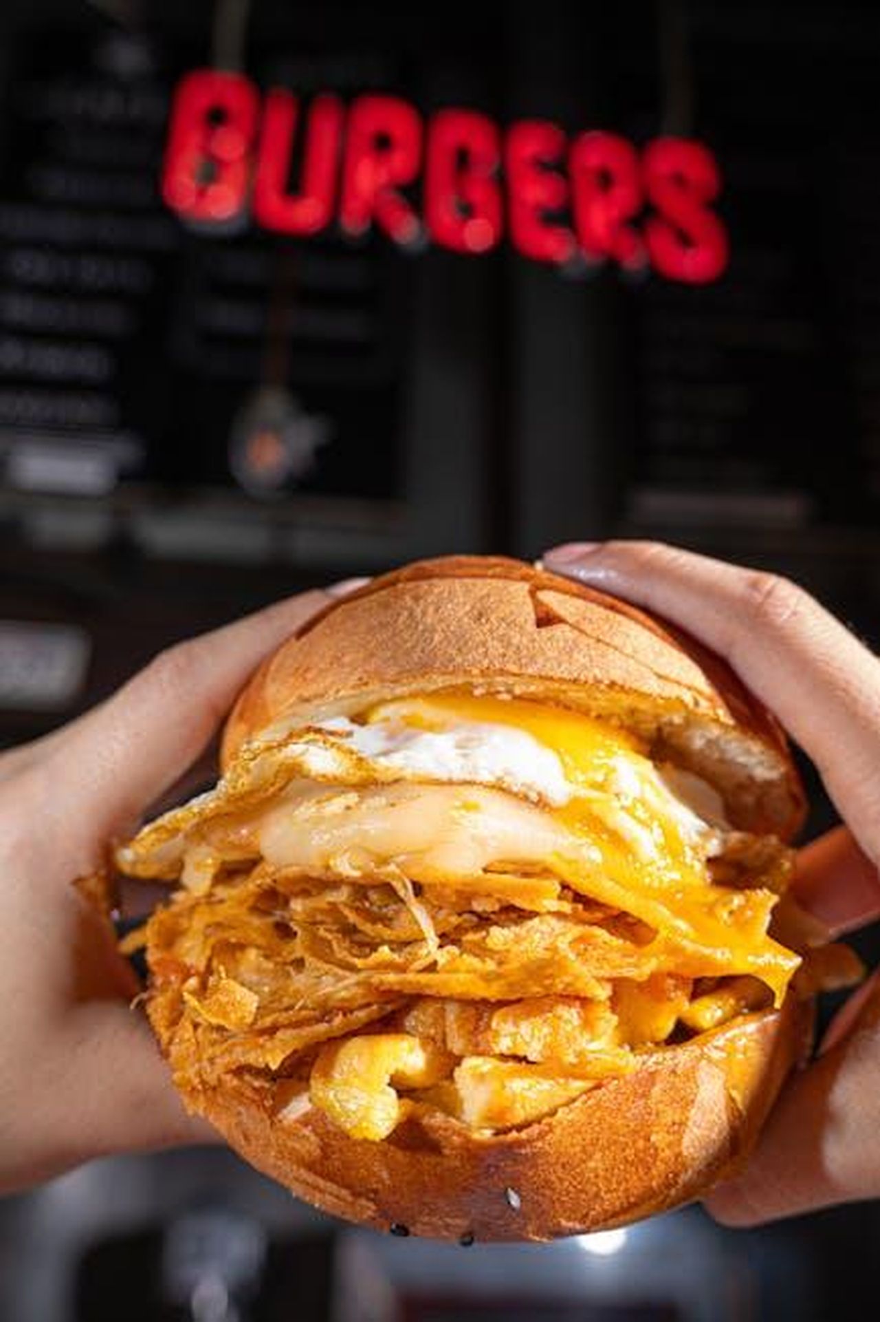 Source: Bon appétit - pexels - Delicious cheesy fried chicken burger topped with a fried egg, held in hands.