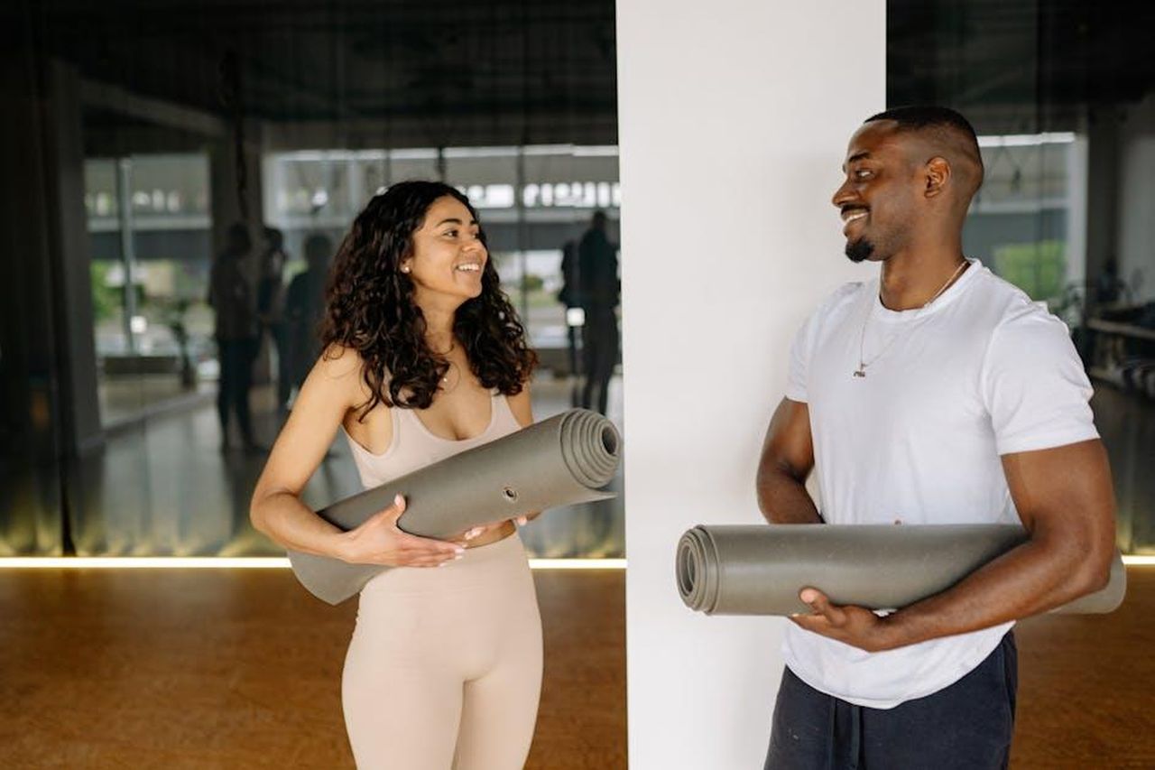 Source: Yan Krukau - pexels - A smiling man and woman holding yoga mats, preparing for a fitness class in a modern gym.