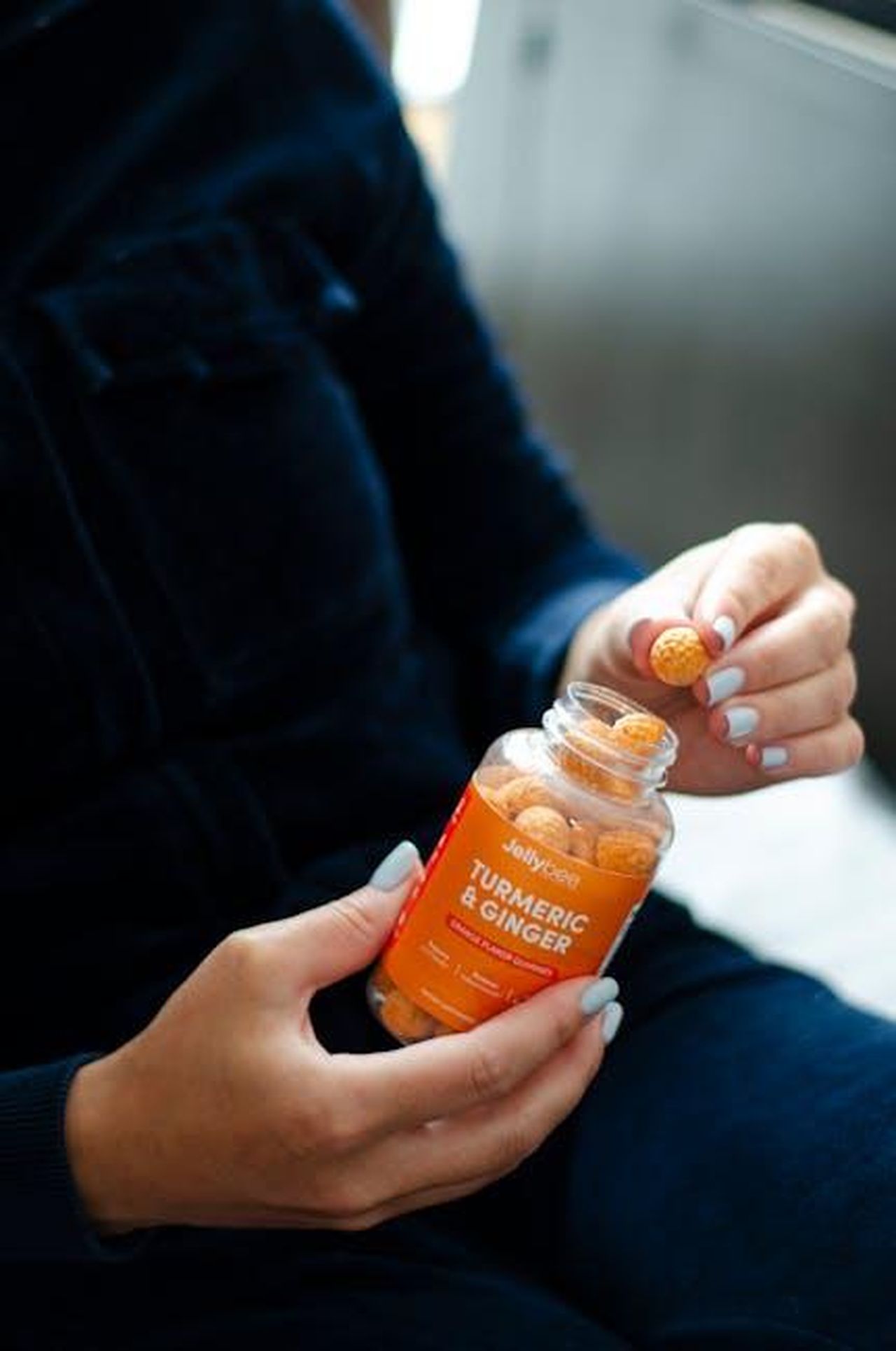 Source: Jellybee - pexels - Close-up of a person holding turmeric and ginger gummies in a bottle with natural lighting.