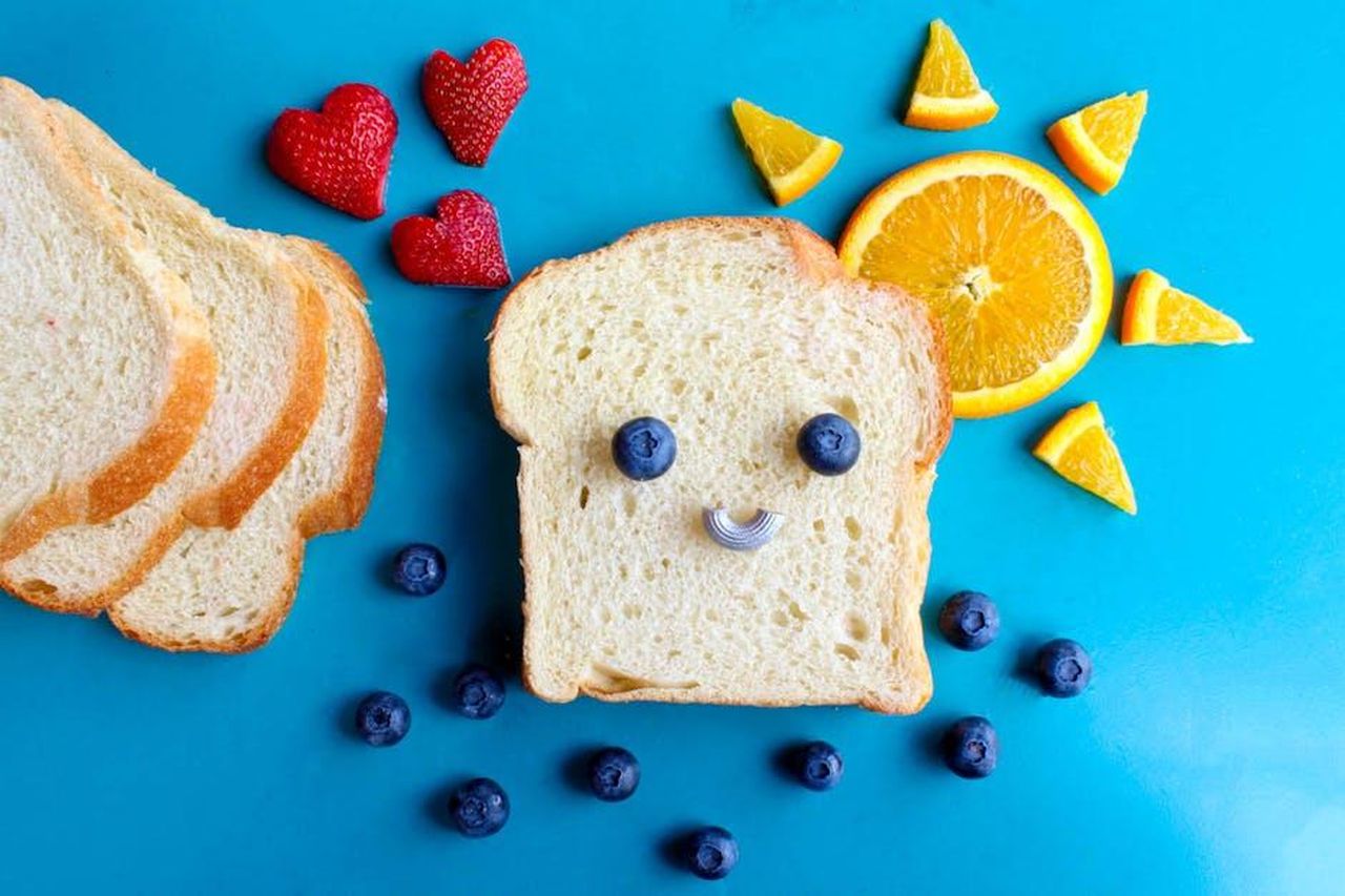 Source: Sydney Troxell - pexels - Fun and colorful toast face art with blueberries, strawberries, and orange slices on a blue background.