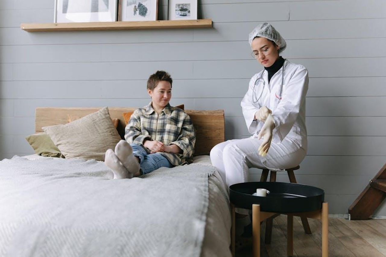 Source: Thirdman - pexels - Patient sits on bed interacting with a doctor in a cozy bedroom environment.