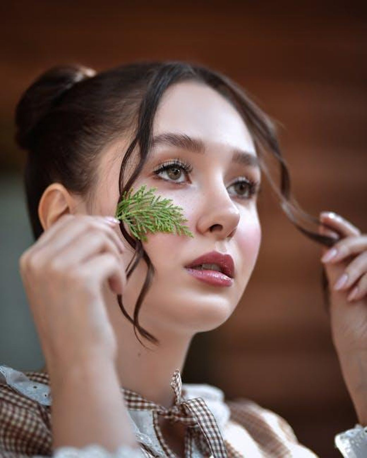 Source: Farzin Yarahmadi - pexels - A serene portrait of a woman holding a thuja leaf, highlighting natural beauty and tranquility.