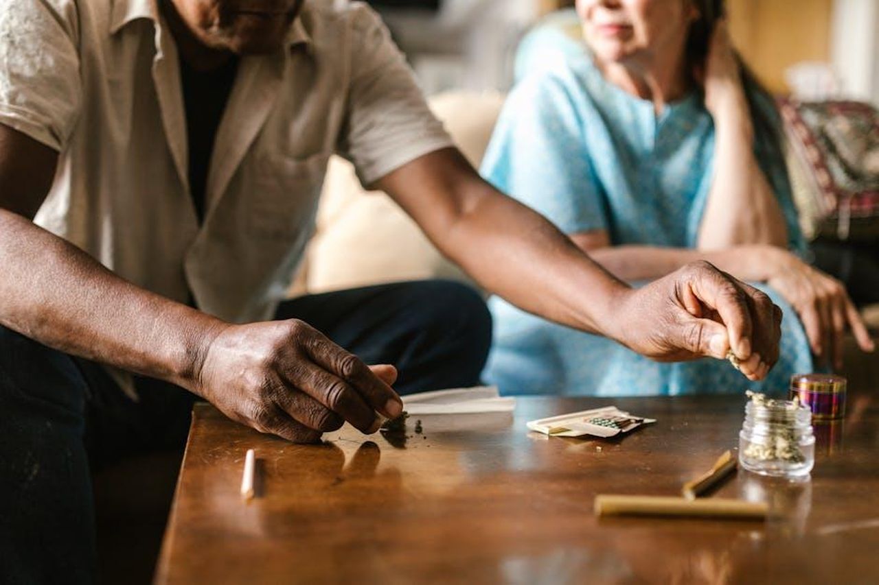 Source: RDNE Stock project - pexels - Two adults preparing cannabis, rolling on a wooden table in a cozy indoor setting.