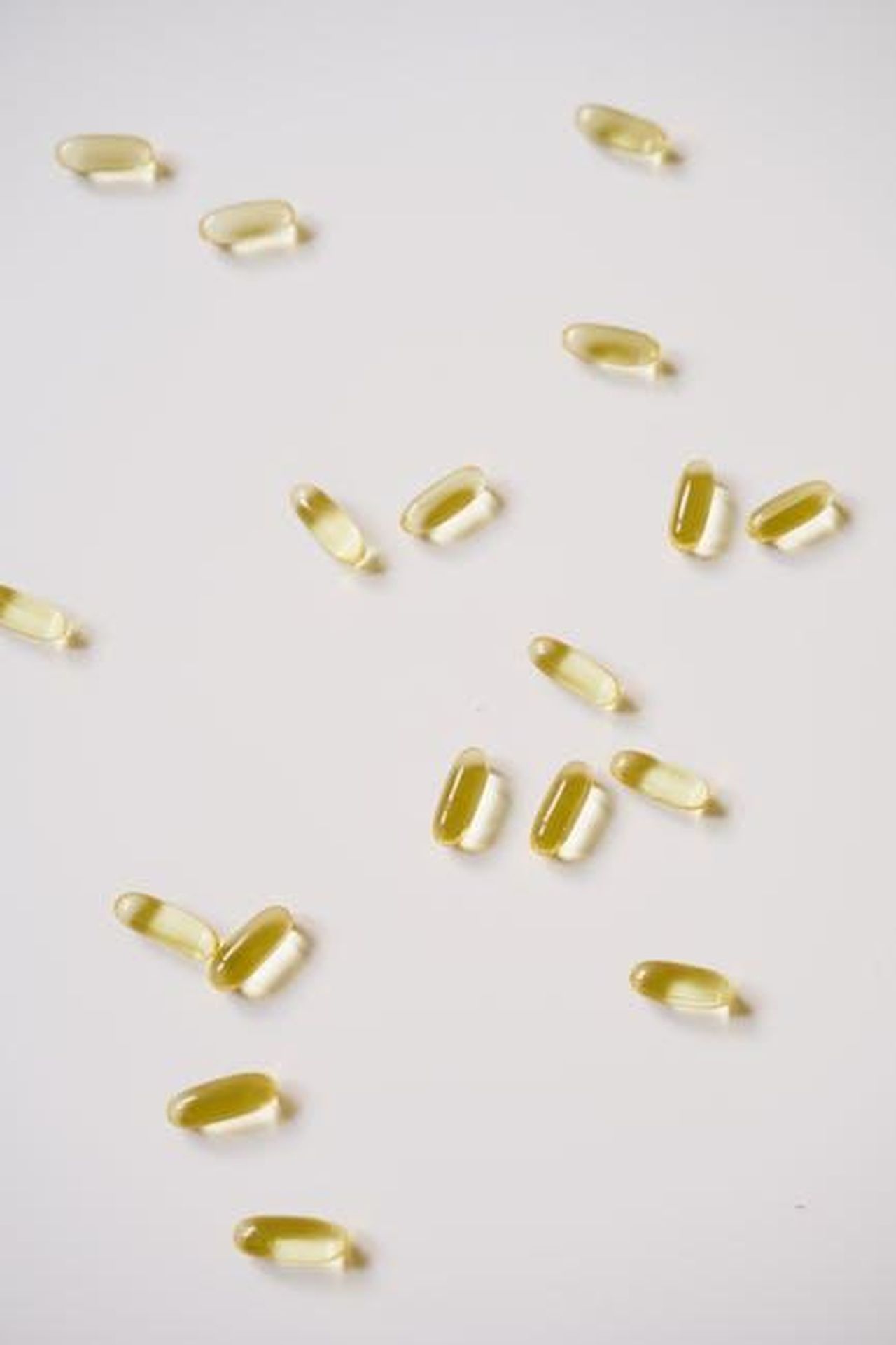 Source: Alesia Kozik - pexels - Close-up of yellow soft gel capsules scattered on a white background, perfect for pharmaceutical themes.