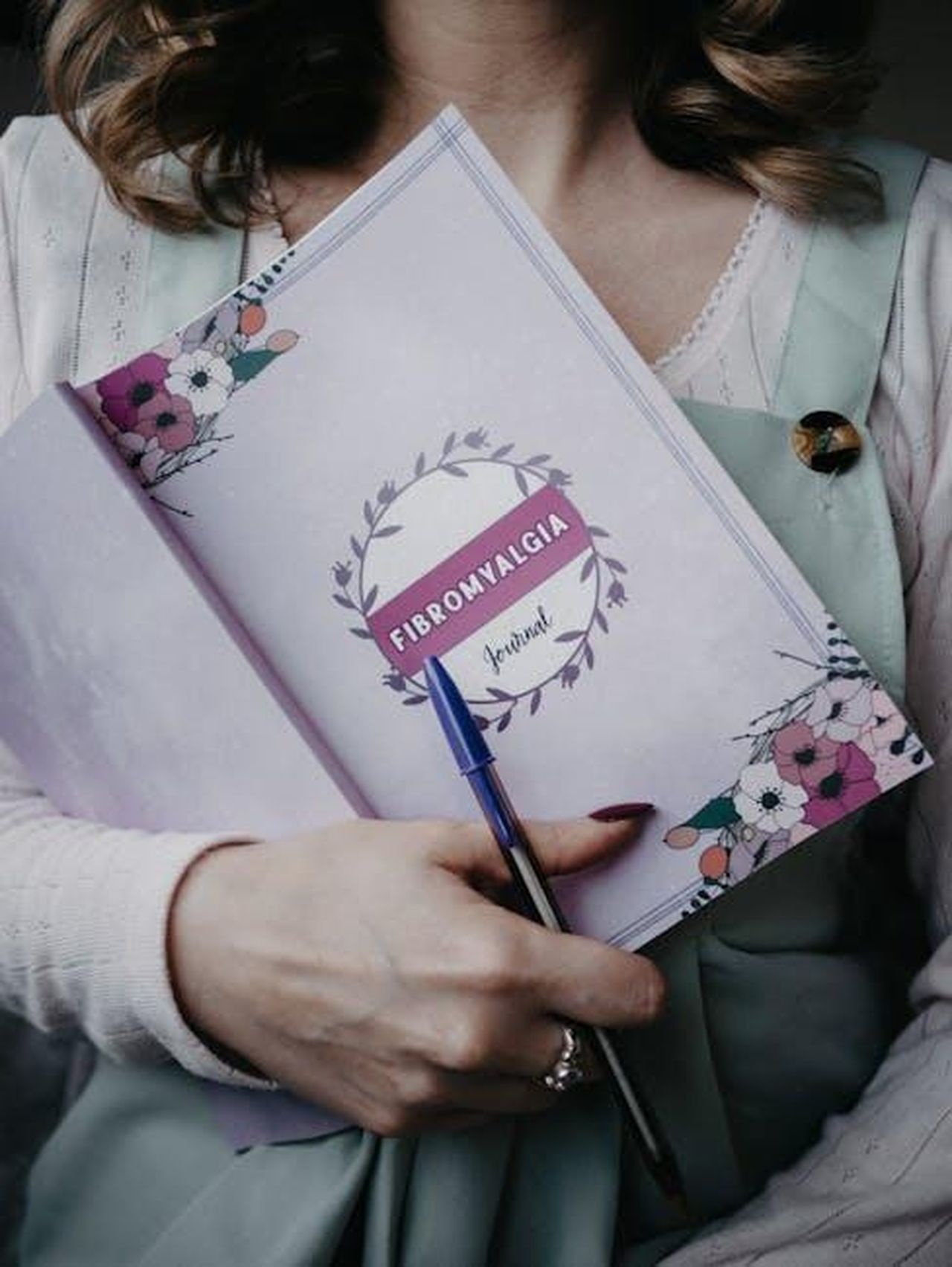 Source: Lisa from Pexels - pexels - A woman holding a fibromyalgia journal with floral design, emphasizing health and awareness.