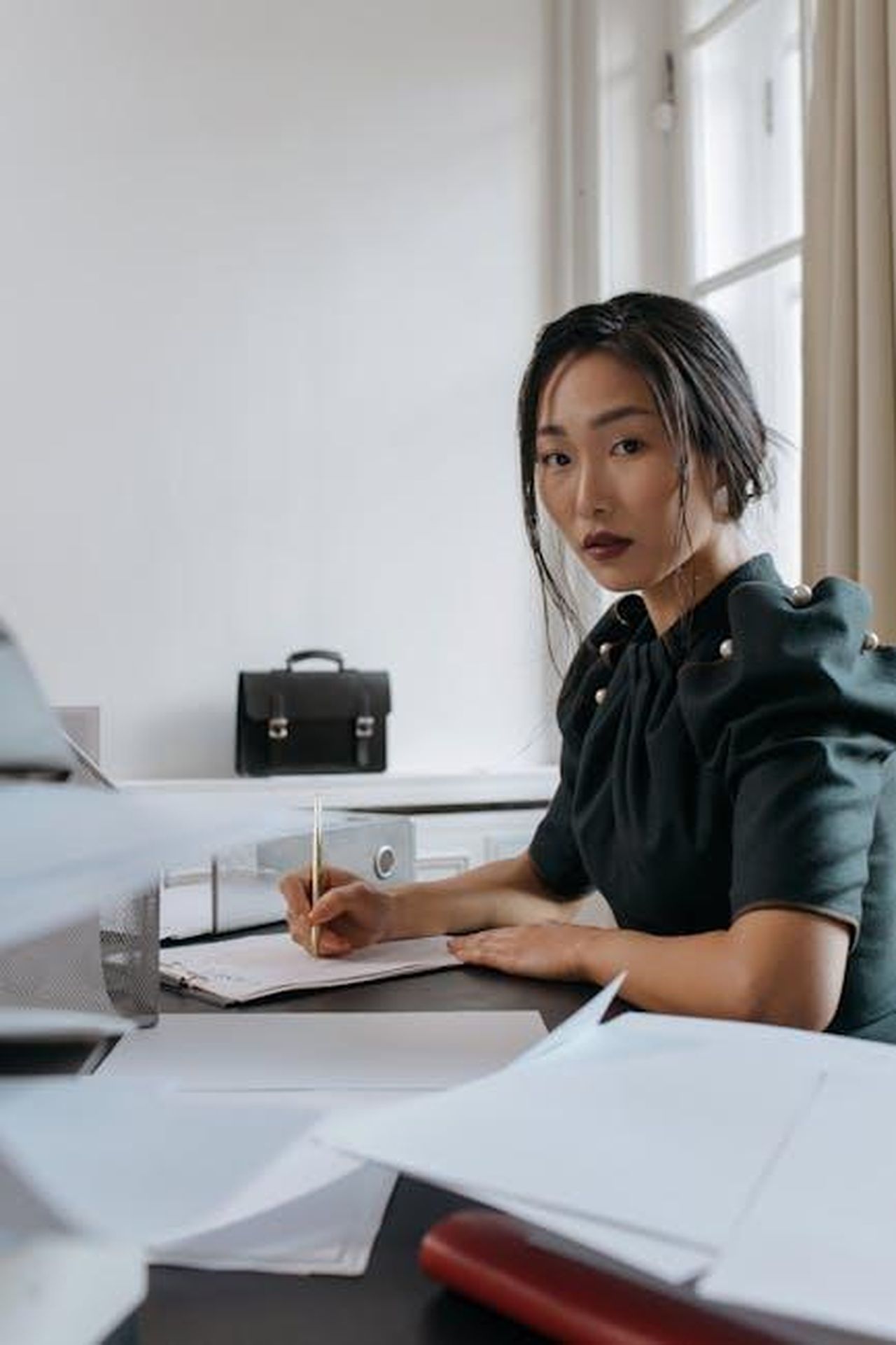 Source: cottonbro studio - pexels - Asian woman focused on paperwork in an office setting, showcasing a modern business environment.