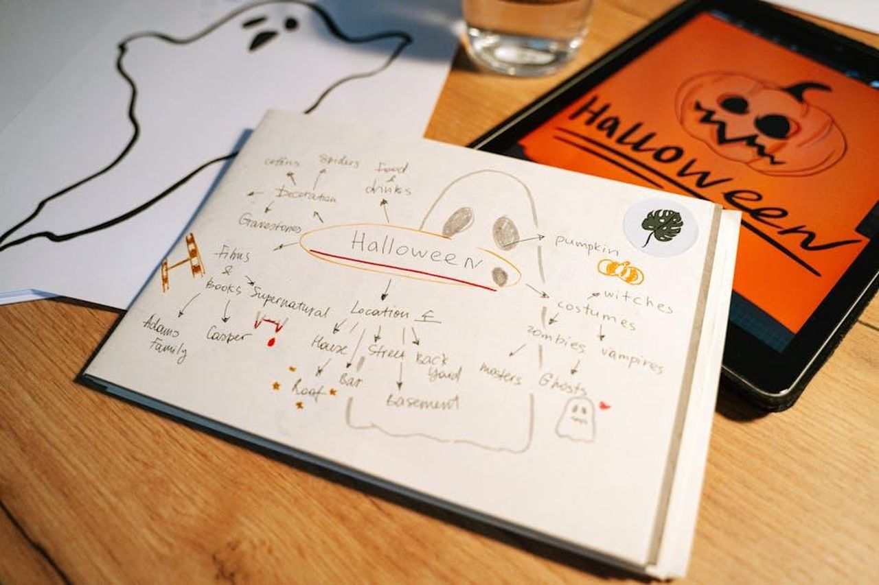 Source: Ivan Samkov - pexels - A Halloween-themed planning session featuring ghost drawings and digital projects on a tablet.