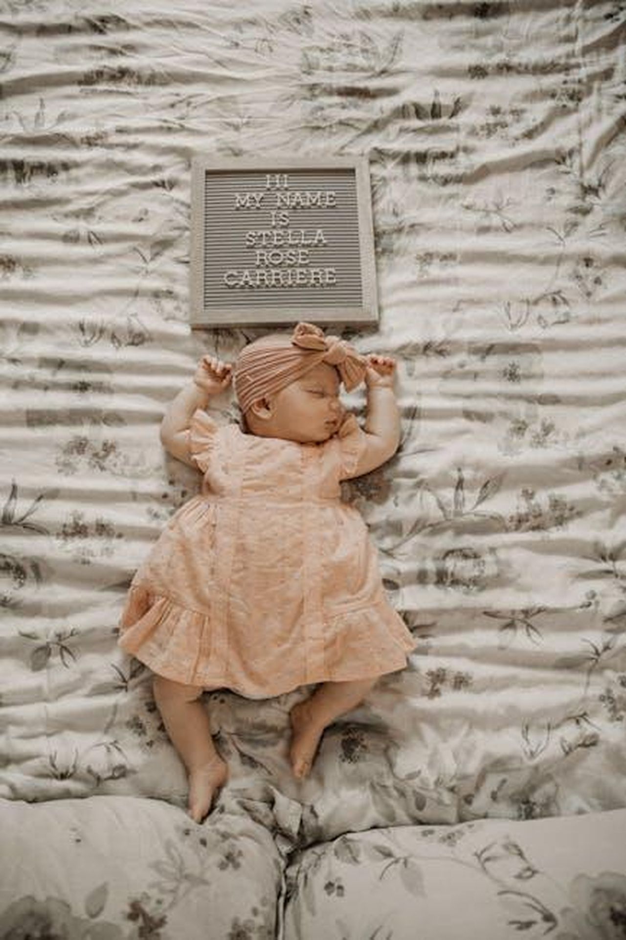 Source: Shottbydani - pexels - Adorable newborn baby girl sleeping peacefully with a name board nearby, captured in a soft and pastel setting.