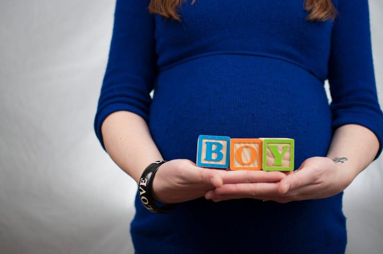 Source: Alicia Zinn - pexels - Pregnant woman in blue dress holds 'boy' blocks, symbolizing a baby boy announcement.