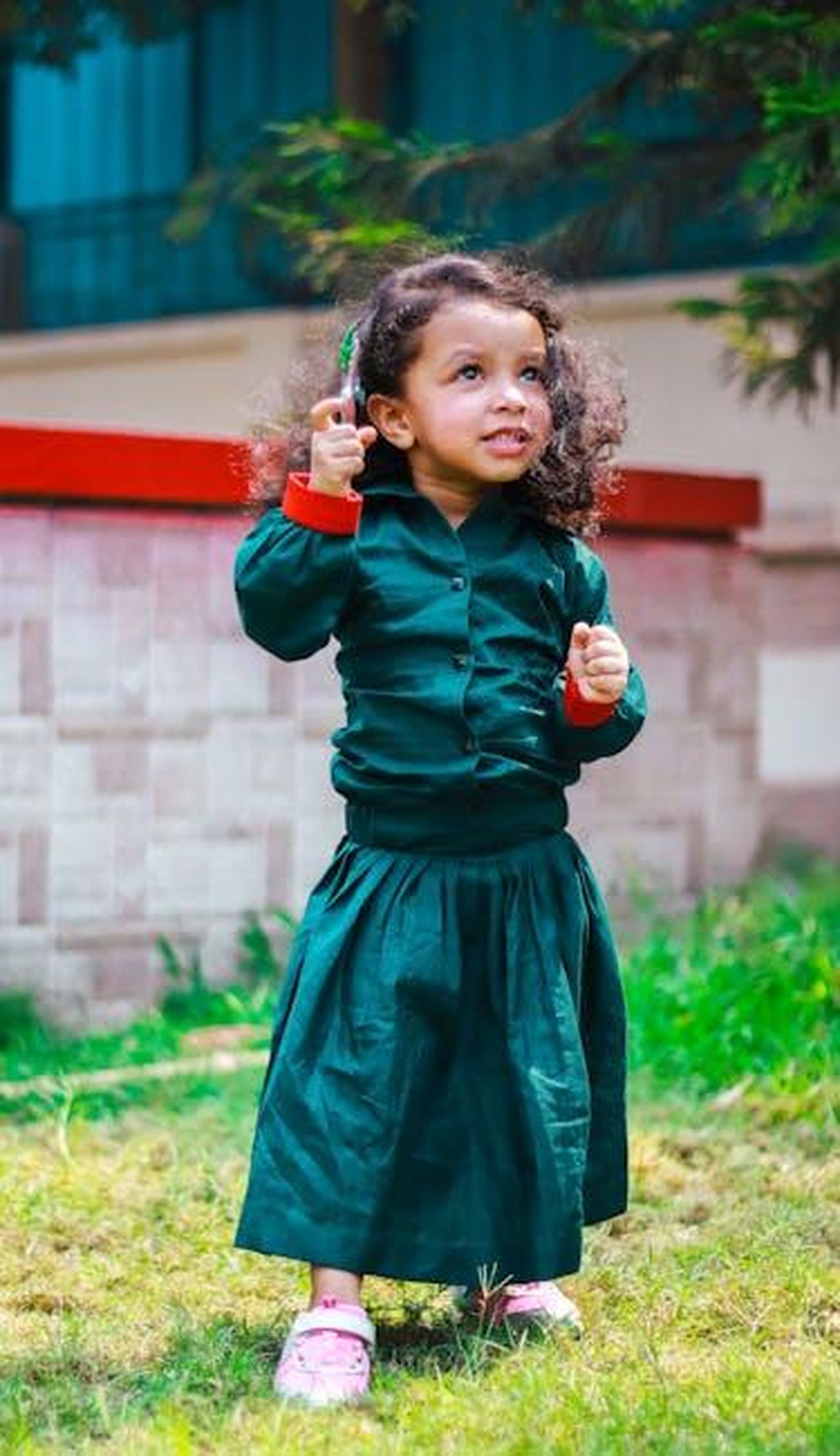 Source: Focus Cam photography - pexels - Charming portrait of a young girl in a green outfit, playing in a sunny garden.