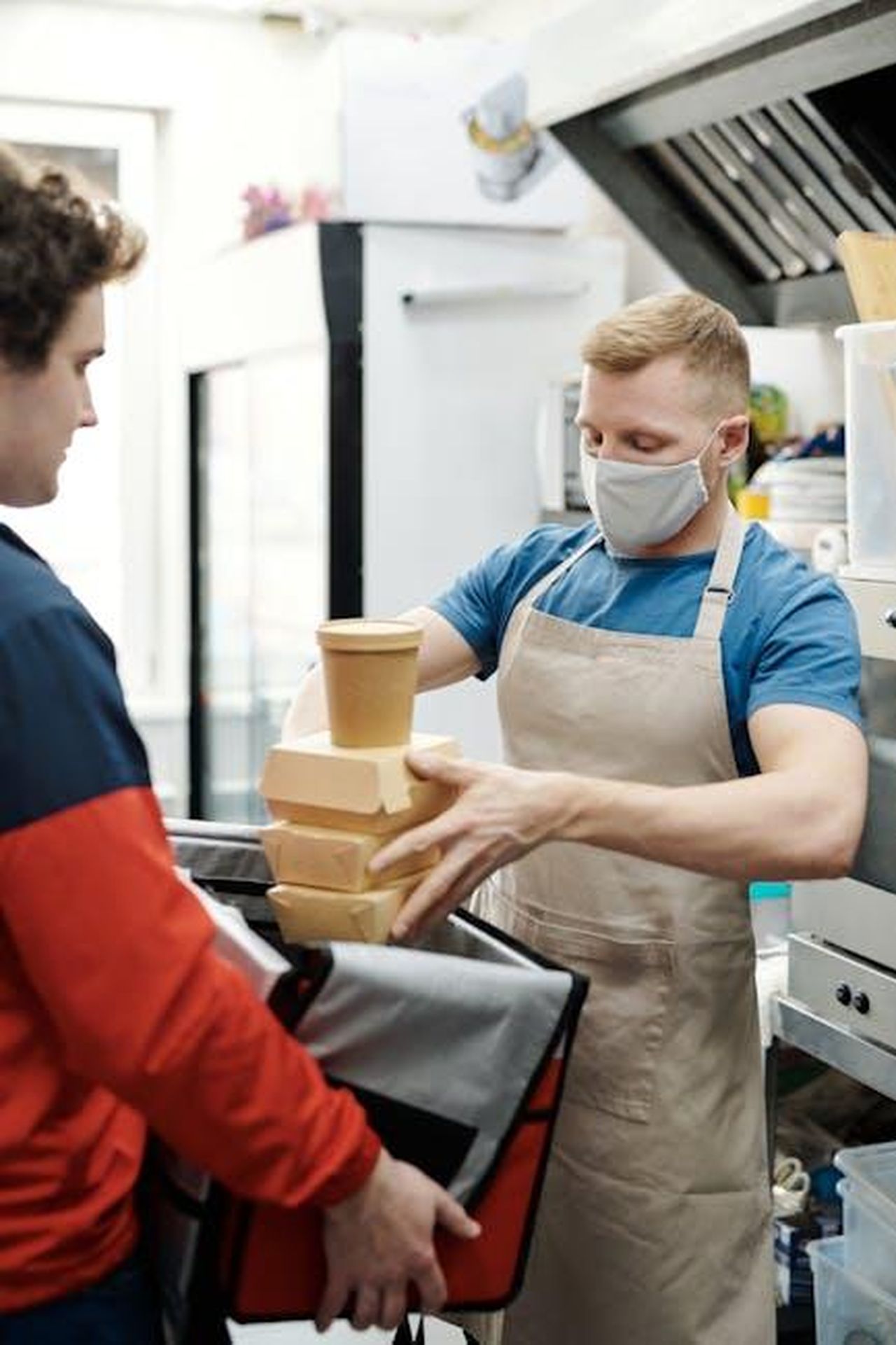 Source: Norma Mortenson - pexels - Masked worker packs takeaway food for delivery in restaurant kitchen.