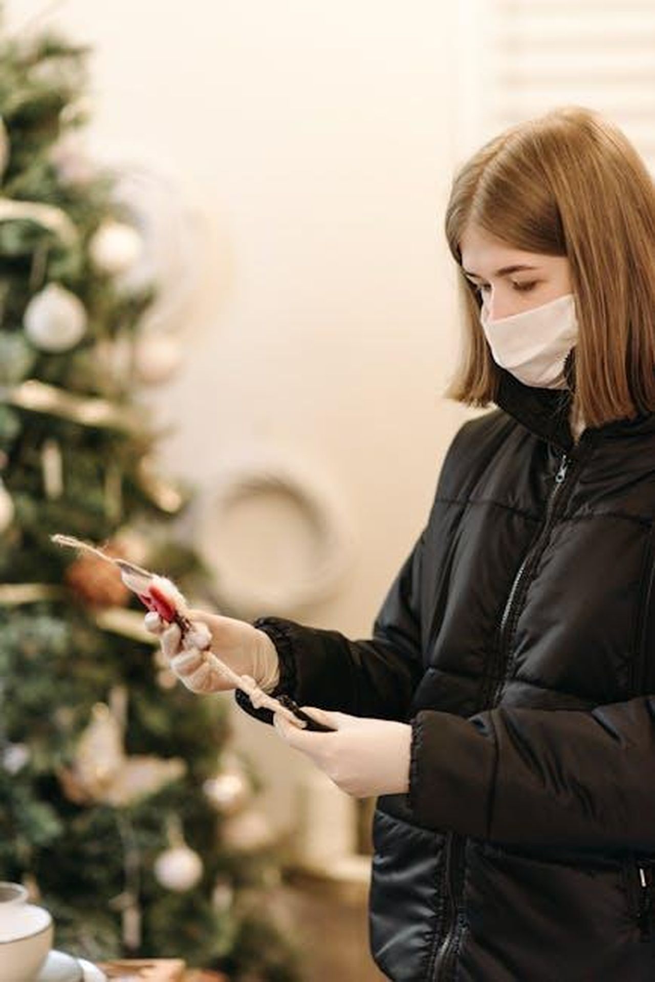 Source: Pavel Danilyuk - pexels - Woman wearing face mask shopping for Christmas decorations indoors with safety precautions.