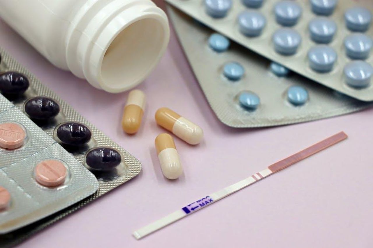 Source: Marta Branco - pexels - Image featuring a pregnancy test strip surrounded by various pills and capsules on a pastel background.