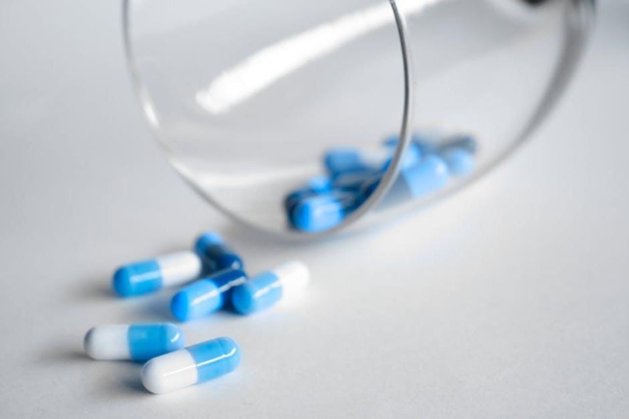 Source: Pietro Jeng - pexels - A close-up of blue and white capsules spilling from a glass on a light background.