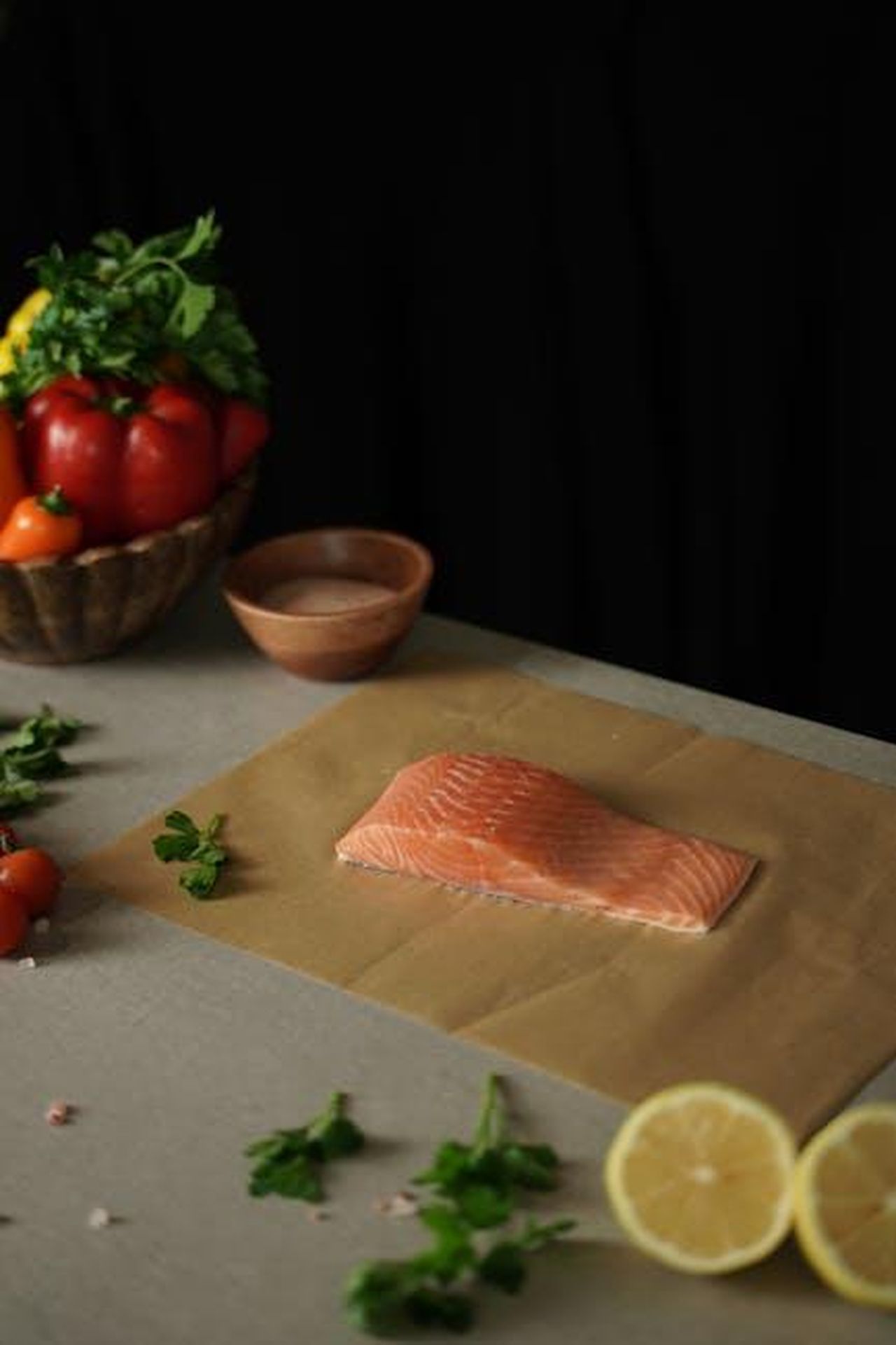 Source: Lalada . - pexels - A fresh salmon fillet on parchment paper with herbs and lemon, ready for cooking.